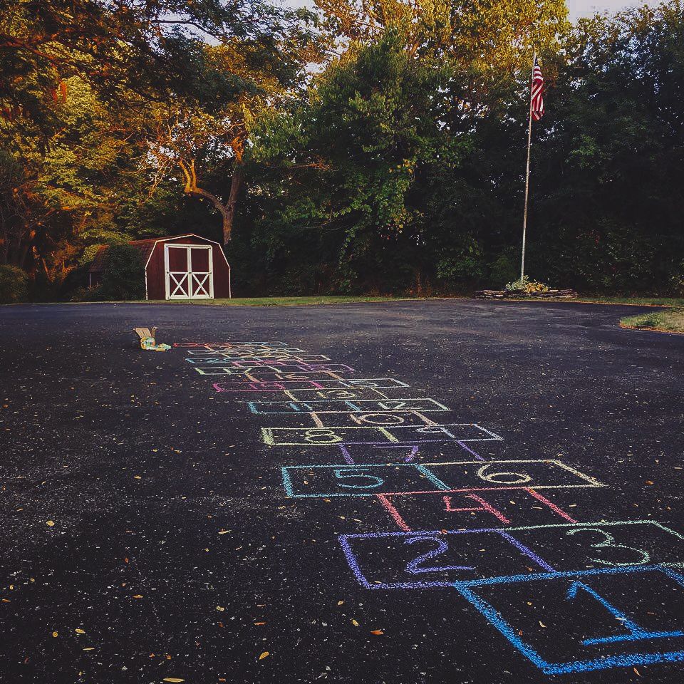 Chalk hopscotch on a driveway with a red shed, candid childhood portrait session, Finger Lakes New York Homestead photography.