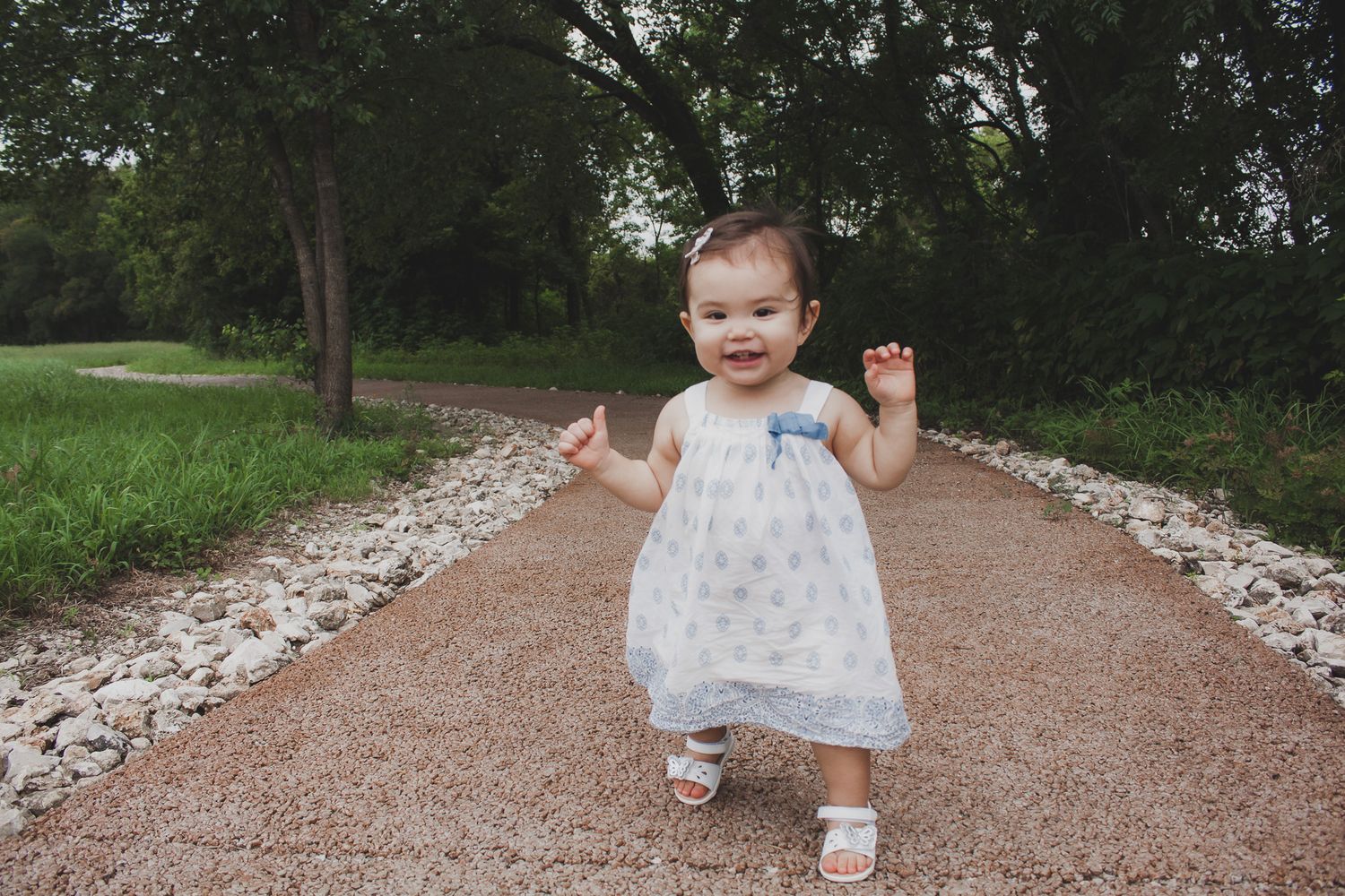 Baby in a white dress walking down a garden stone path, candid outdoor portrait, Finger Lakes NY, Soft Wild Light.
