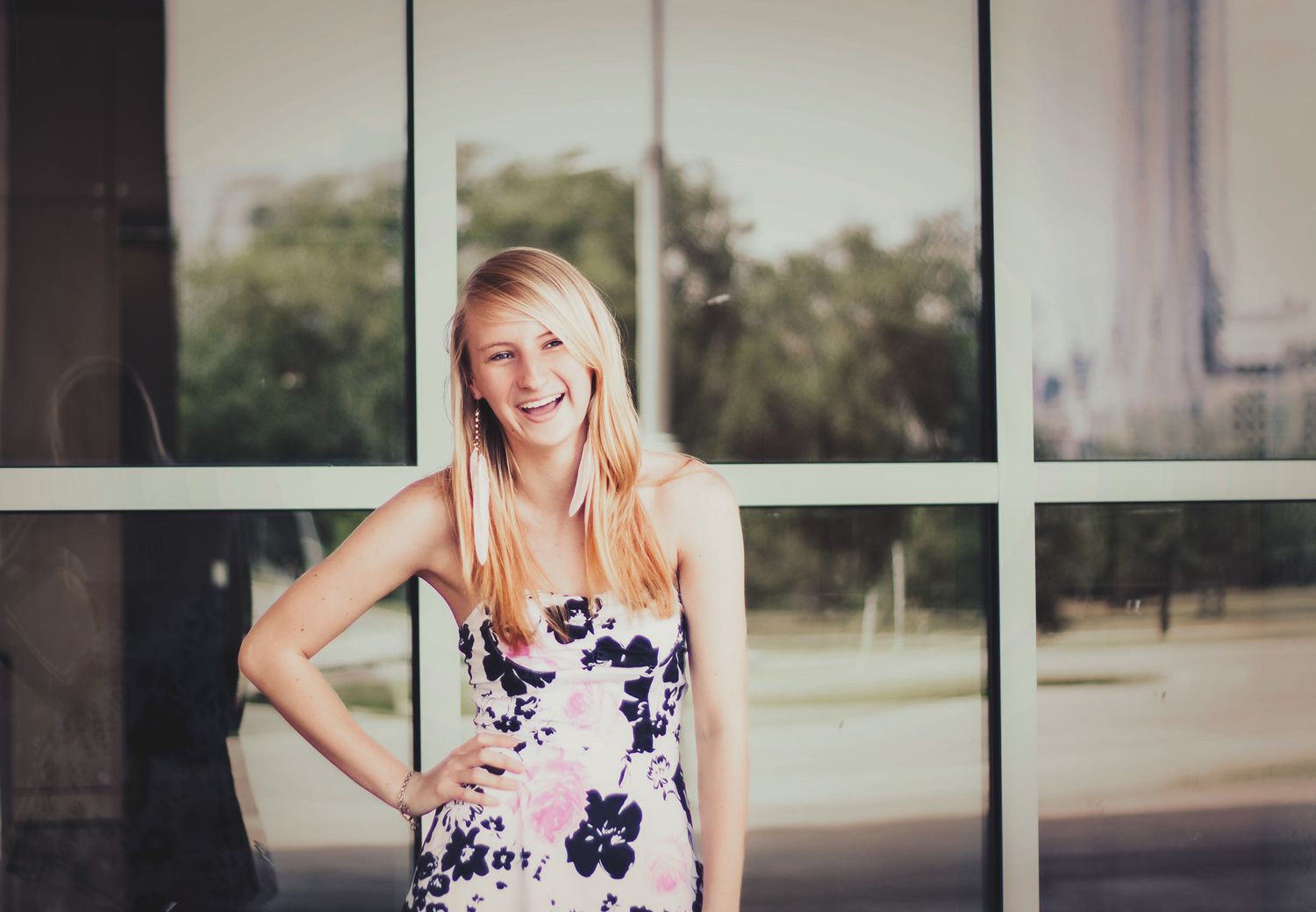 Senior portrait of a teenage girl in a floral dress posed against large windows, natural light photography, Finger Lakes NY