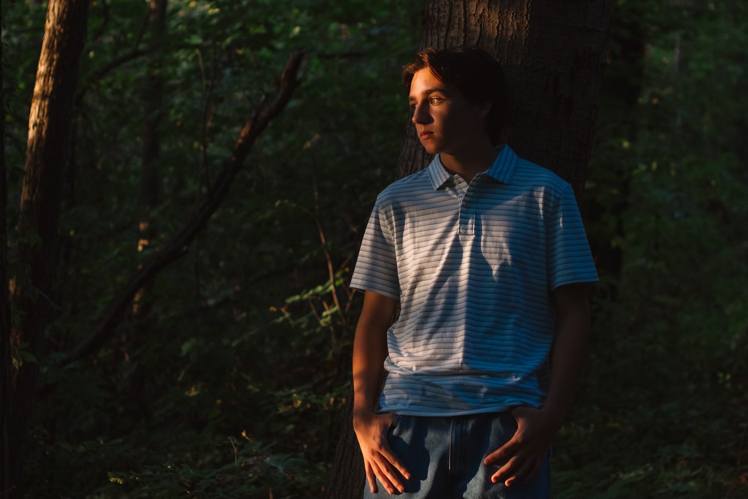 Dramatic senior portrait of a teenage boy in a dark wooded outdoor setting, natural light photography, Finger Lakes NY, Soft Wild Light