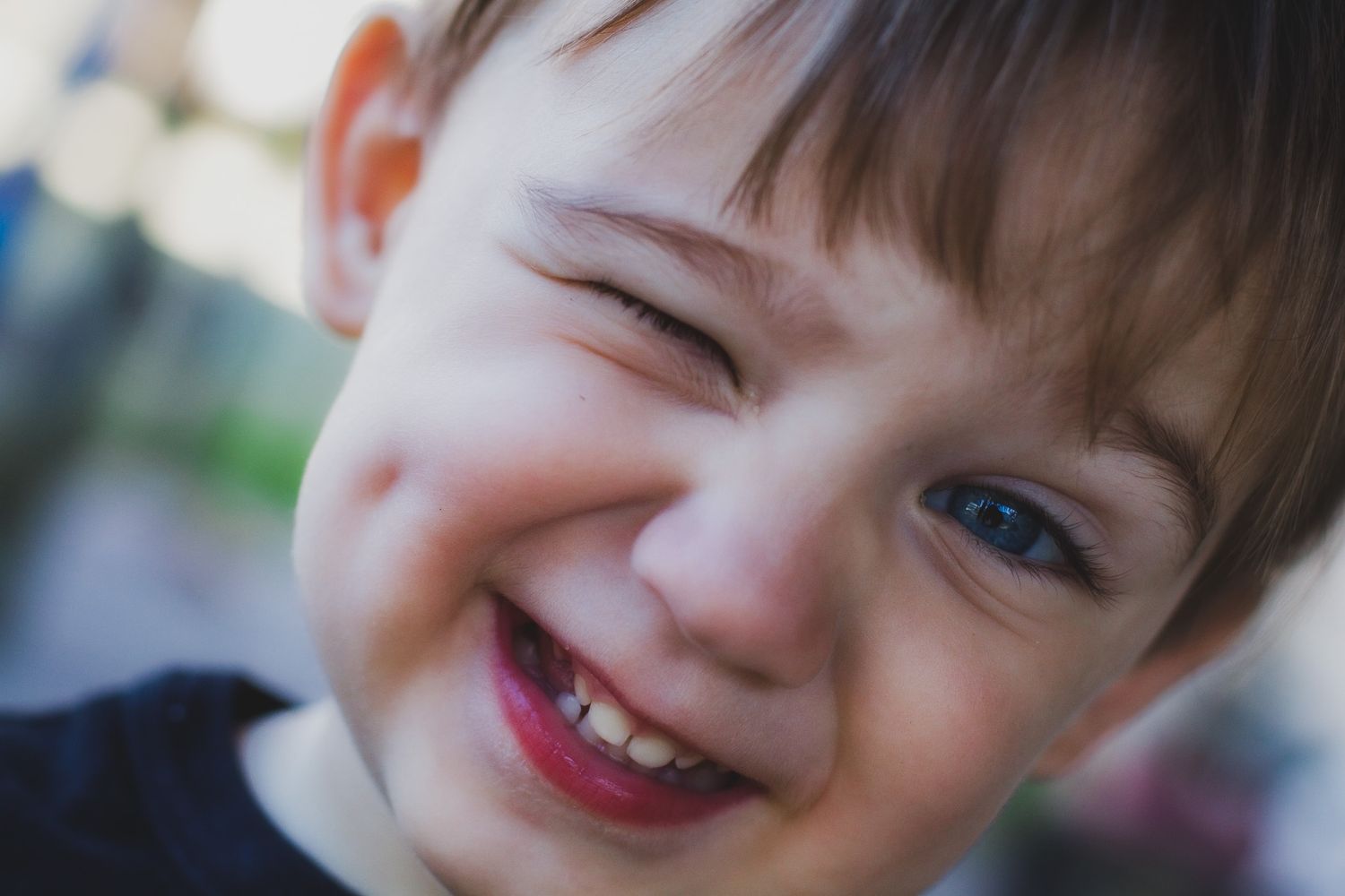 Close up portrait of a laughing young child winking in natural light, candid child photography, Finger Lakes NY, Soft Wild Light.