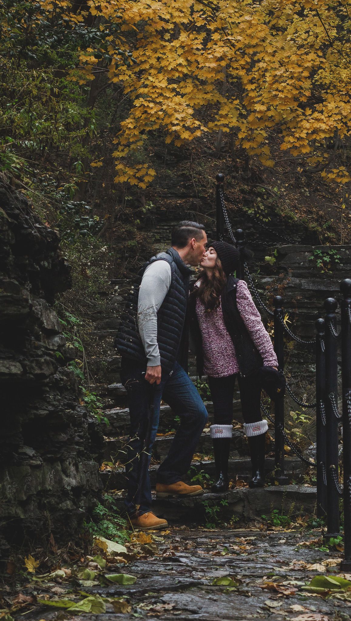 Engaged couple standing close together kissing near water surrounded by autumn foliage, outdoor engagement portrait session, Finger Lakes NY