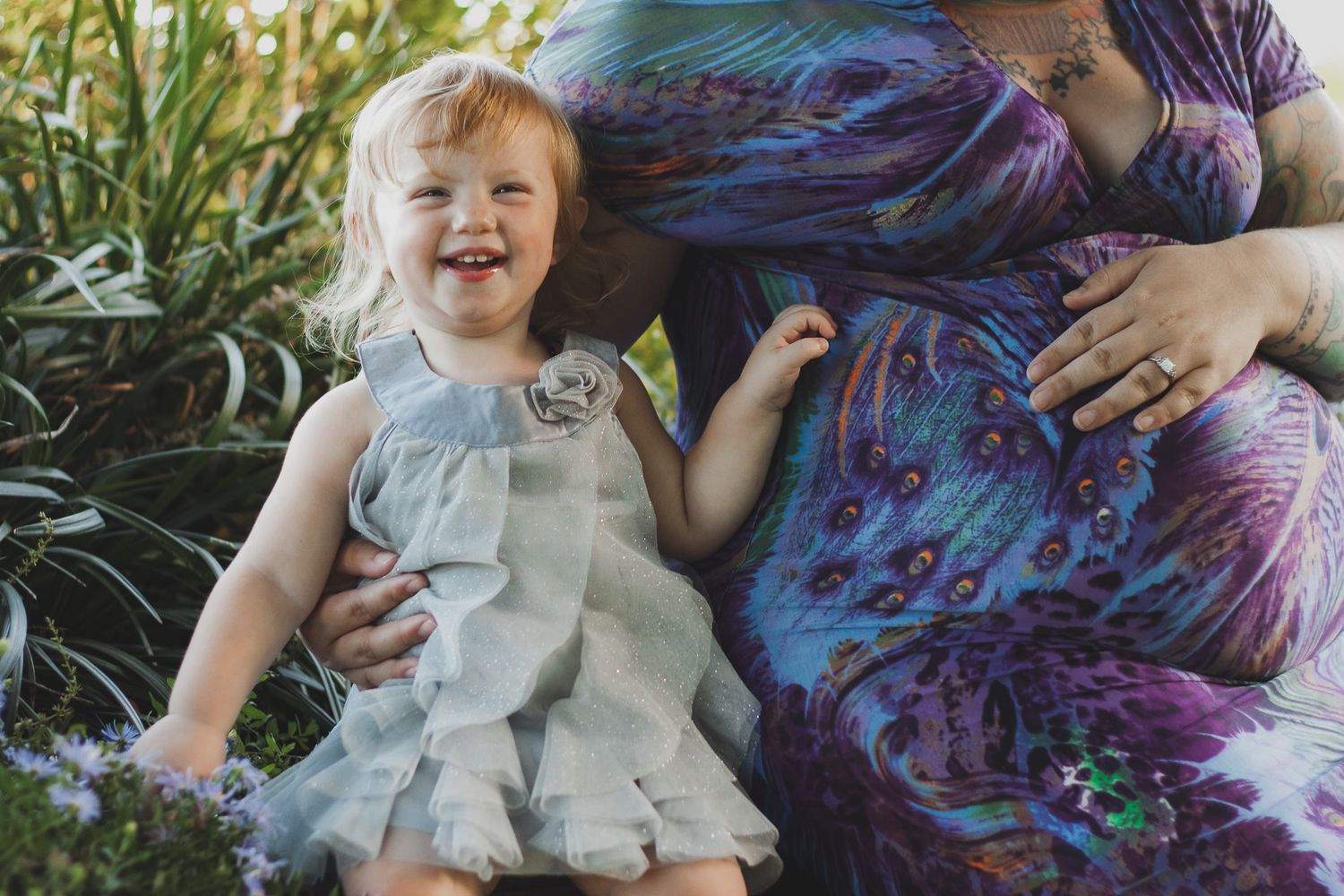 Laughing toddler girl held by a pregnant mother in a lush garden, candid natural light portrait, Finger Lakes NY, Soft Wild Light.