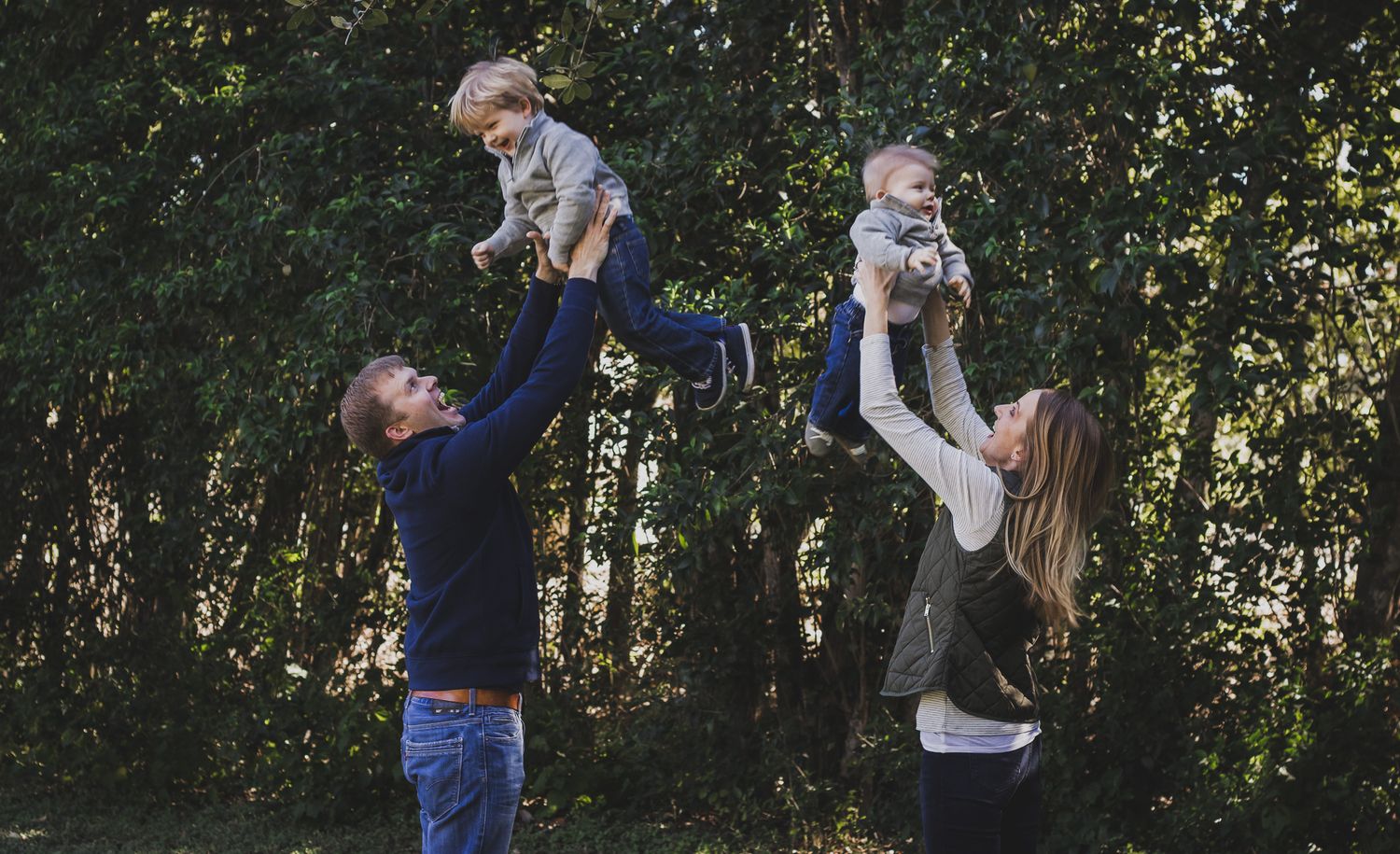 Parents playfully lifting babies in the air under trees, candid family portrait, Finger Lakes NY, Michelle Lawson Photographer.