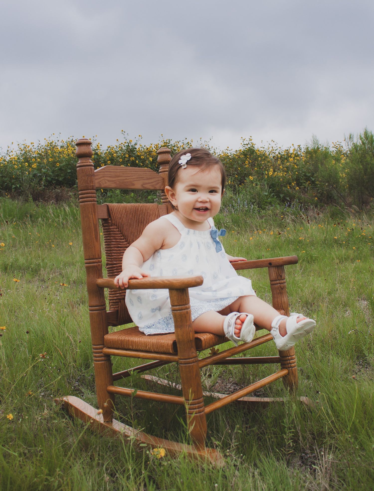Baby sitting in a wooden rocking chair outdoors in a wildflower field, natural light outdoor portrait, Finger Lakes NY, Soft Wild Light.