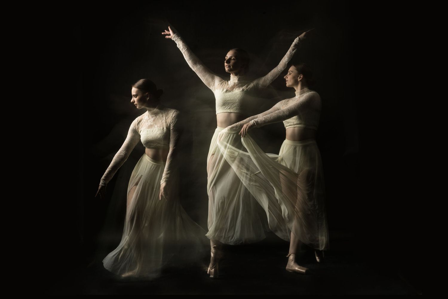 Dancers in flowing white costumes perform graceful movements against a dark background in a series of artistic poses.