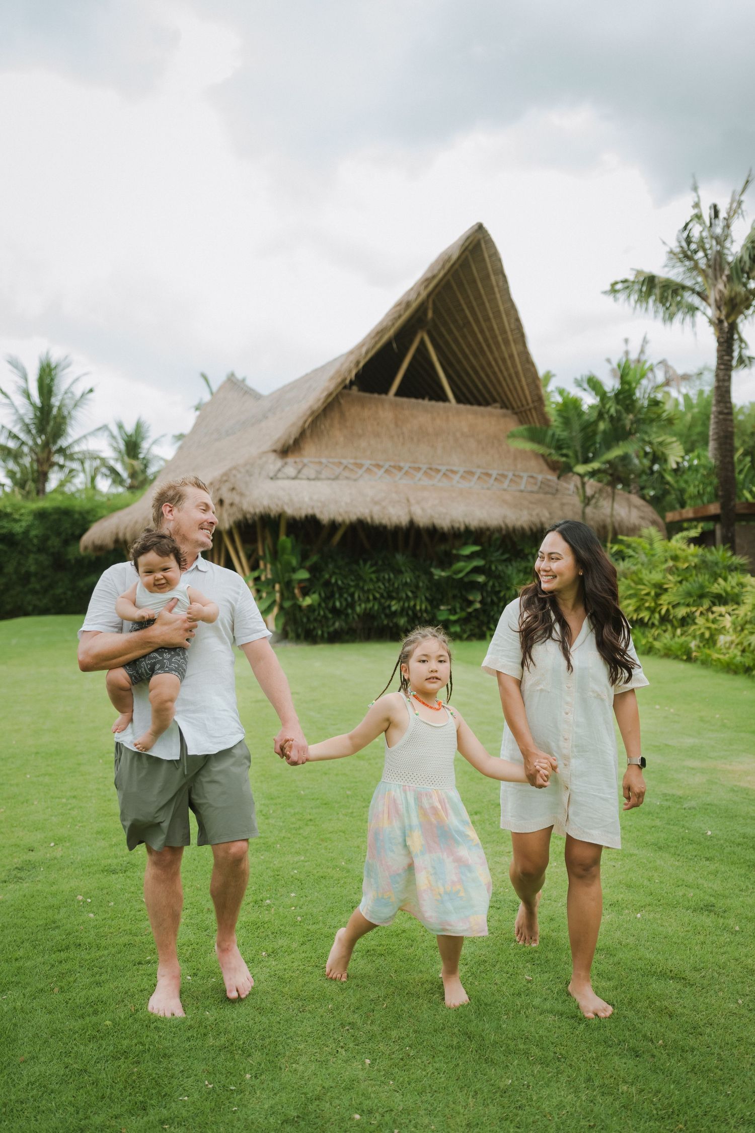 Family walking and playing together on a lush green lawn with tropical palm trees in the background.
