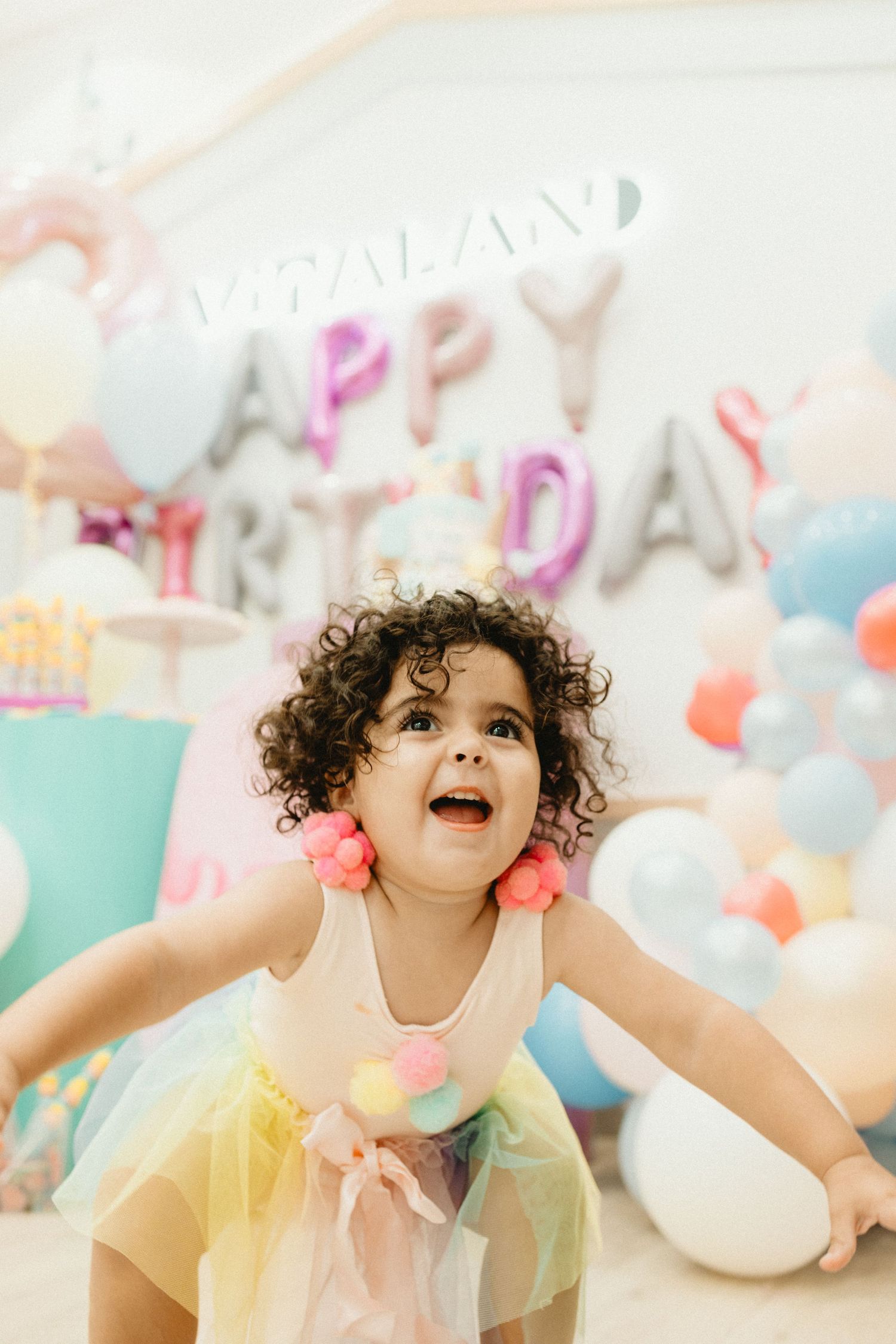 A joyful celebration with colorful balloons and a 'Happy Birthday' banner in pastel tones creates a festive party atmosphere.