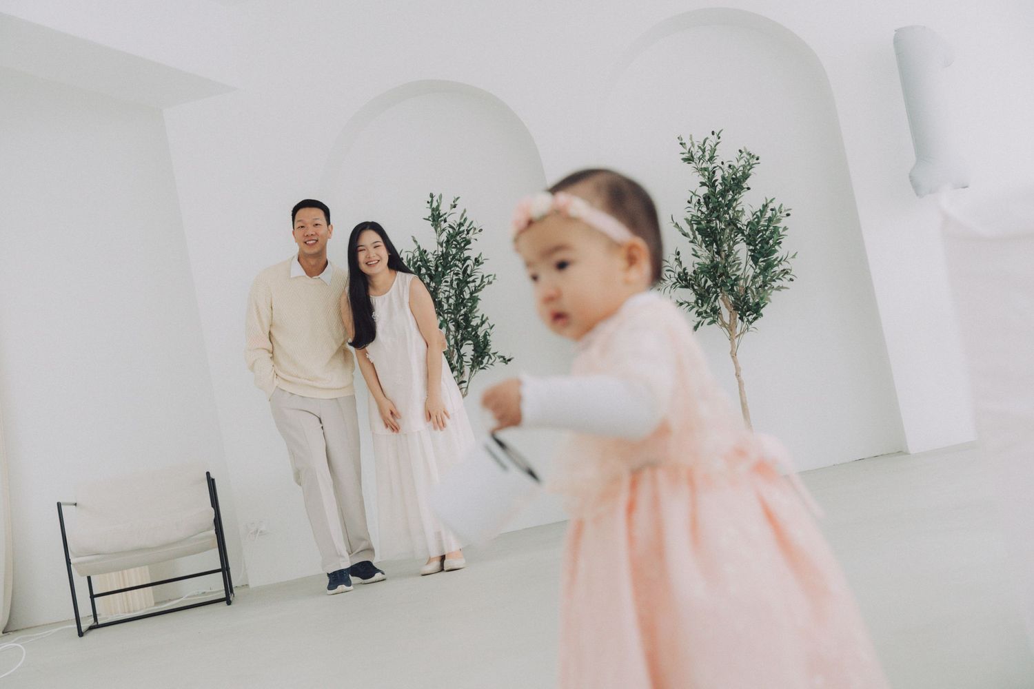 A minimalist white studio photoshoot featuring soft pink accents and greenery decorations.