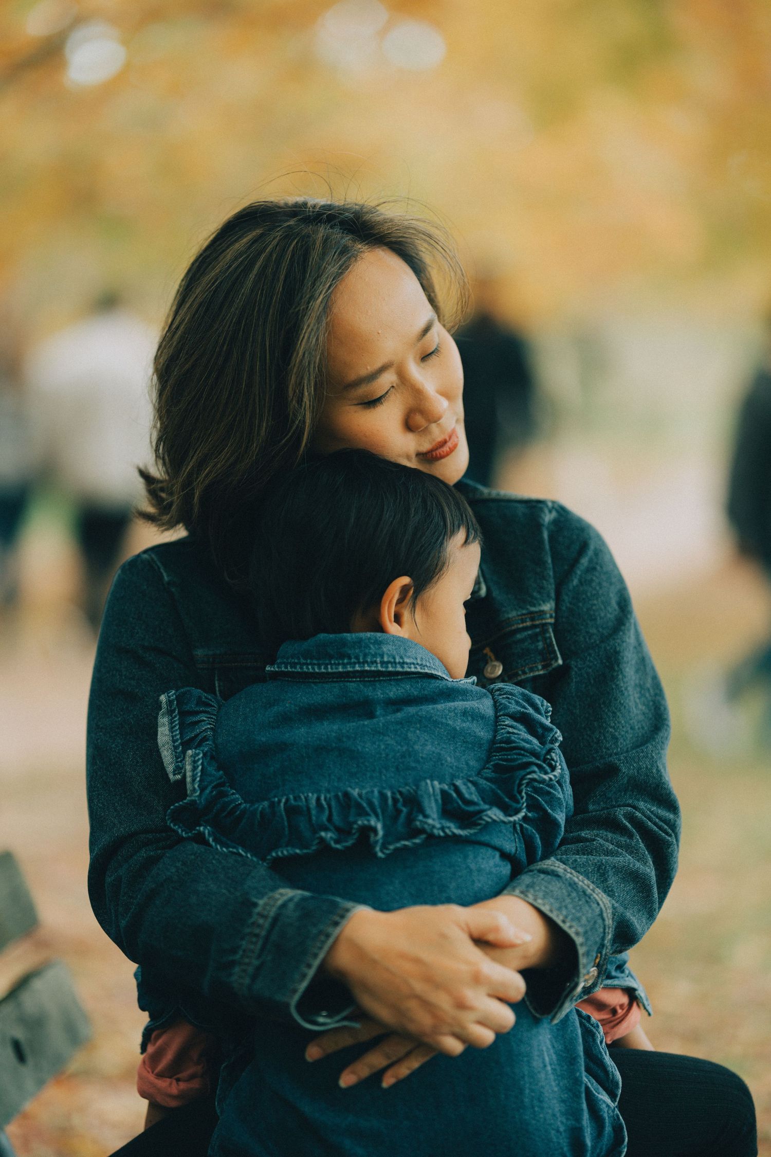 Two people wearing denim embrace in a tender moment during autumn with blurred golden foliage in the background.