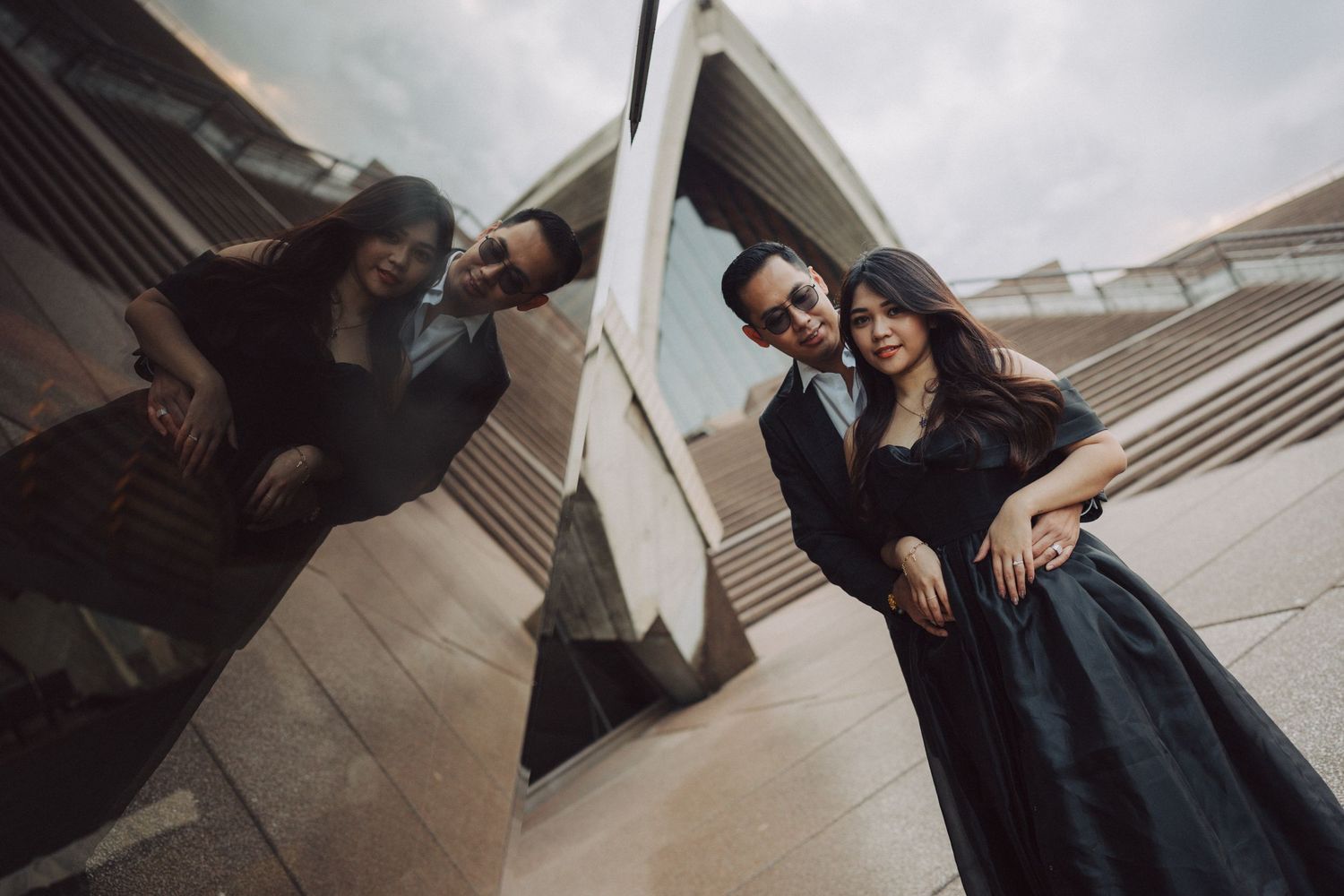 A couple in dark formal attire poses intimately on concrete steps during an outdoor photo session.