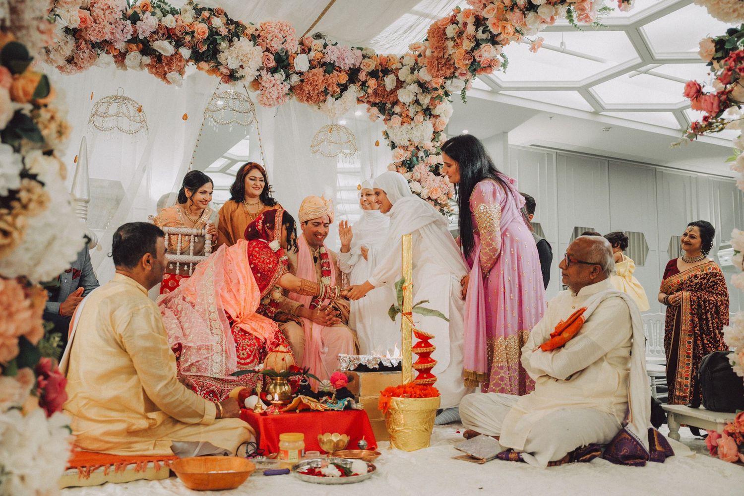Colorful Indian wedding ceremony with floral arch, guests in traditional attire, and ritual offerings on the floor.