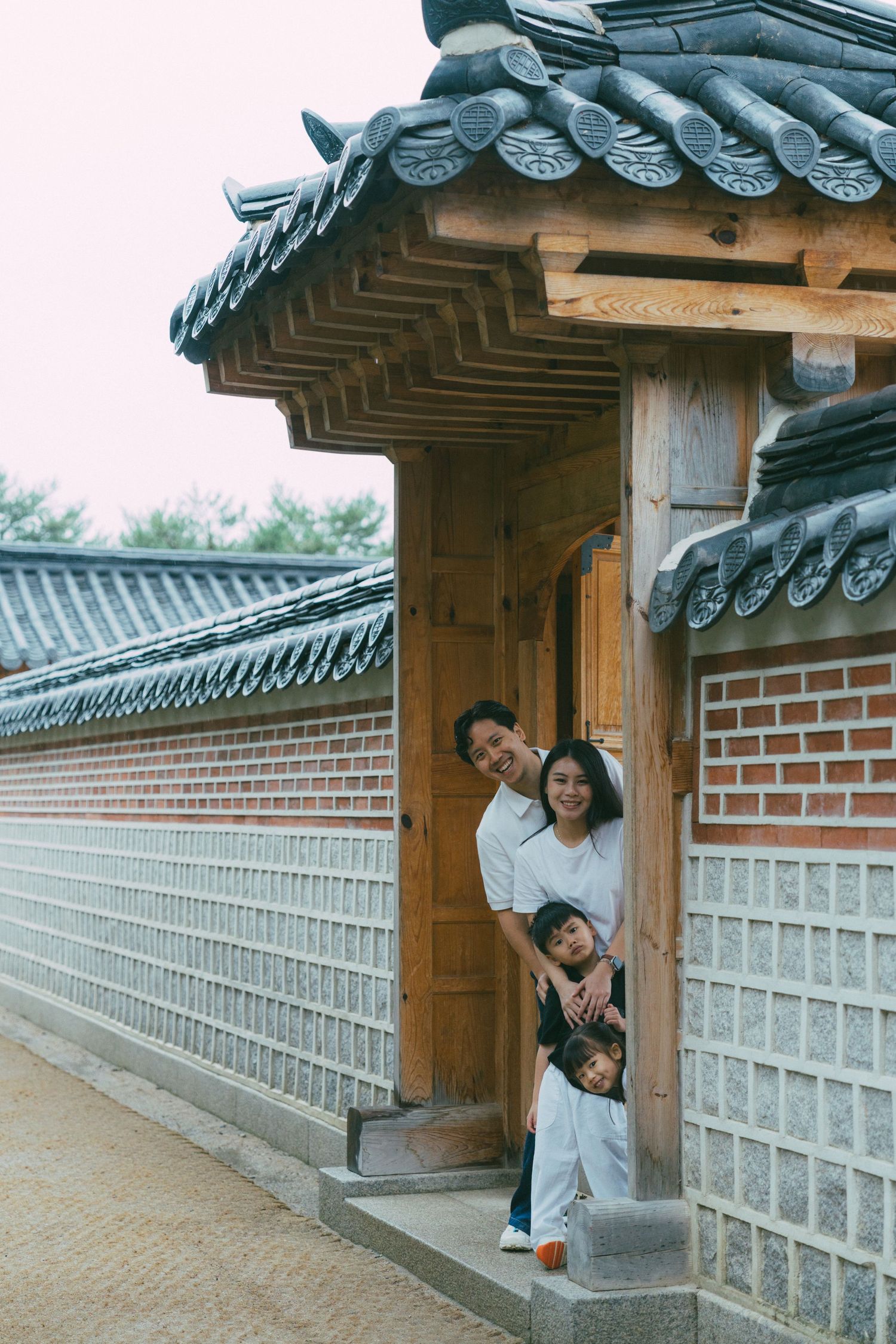 A series of photos showing people posing playfully along a traditional Korean stone wall with curved tile roof architecture.