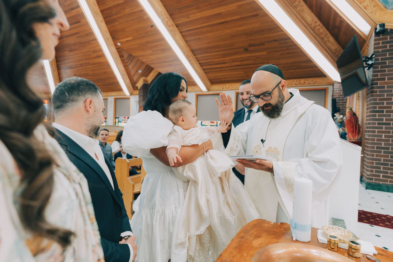 A group of people in white robes perform a religious ceremony in a church with wooden beams and brick walls.