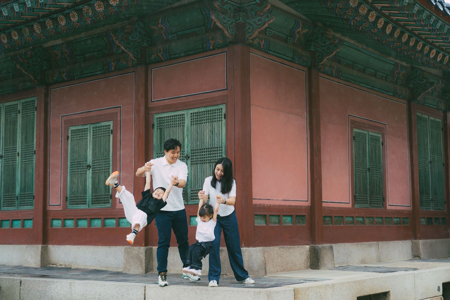 Children play and explore around traditional Korean temple buildings with red pillars and green rooftops.