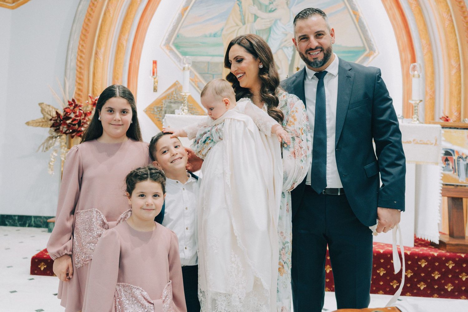Wedding party in pink and gray attire poses together in elegant church setting with ornate arches and columns.