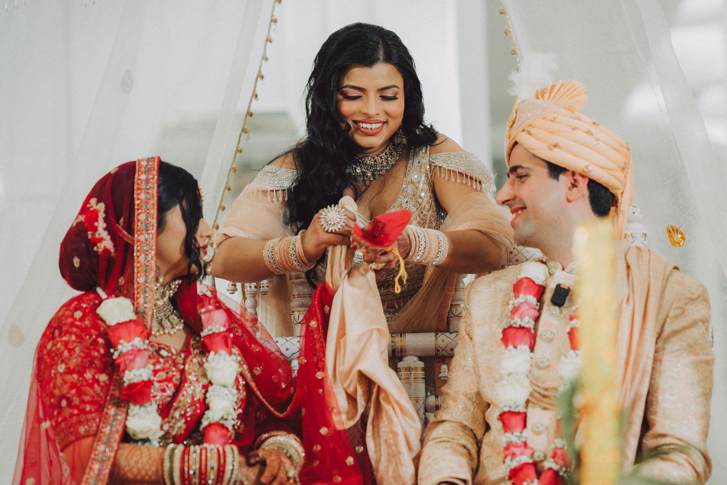 Bride and groom in traditional Indian wedding attire during ceremony ritual with officiant in red and gold outfits.