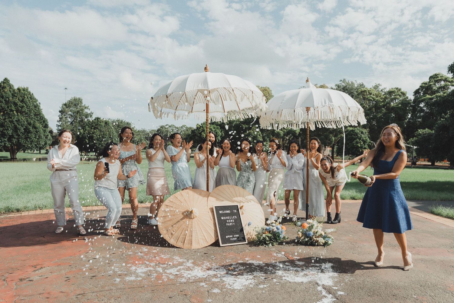 Wedding party members walk with decorative white parasols on a sunny day during an outdoor celebration.
