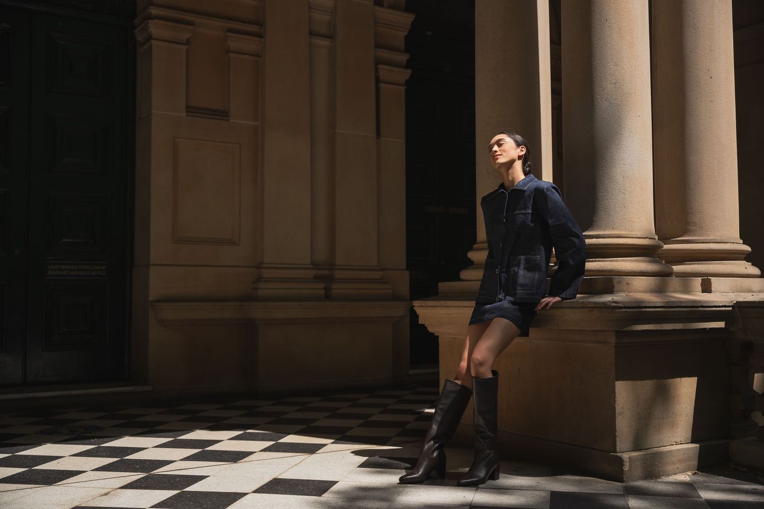 Person sits in shadows on stone steps between classical columns in dramatic lighting.
