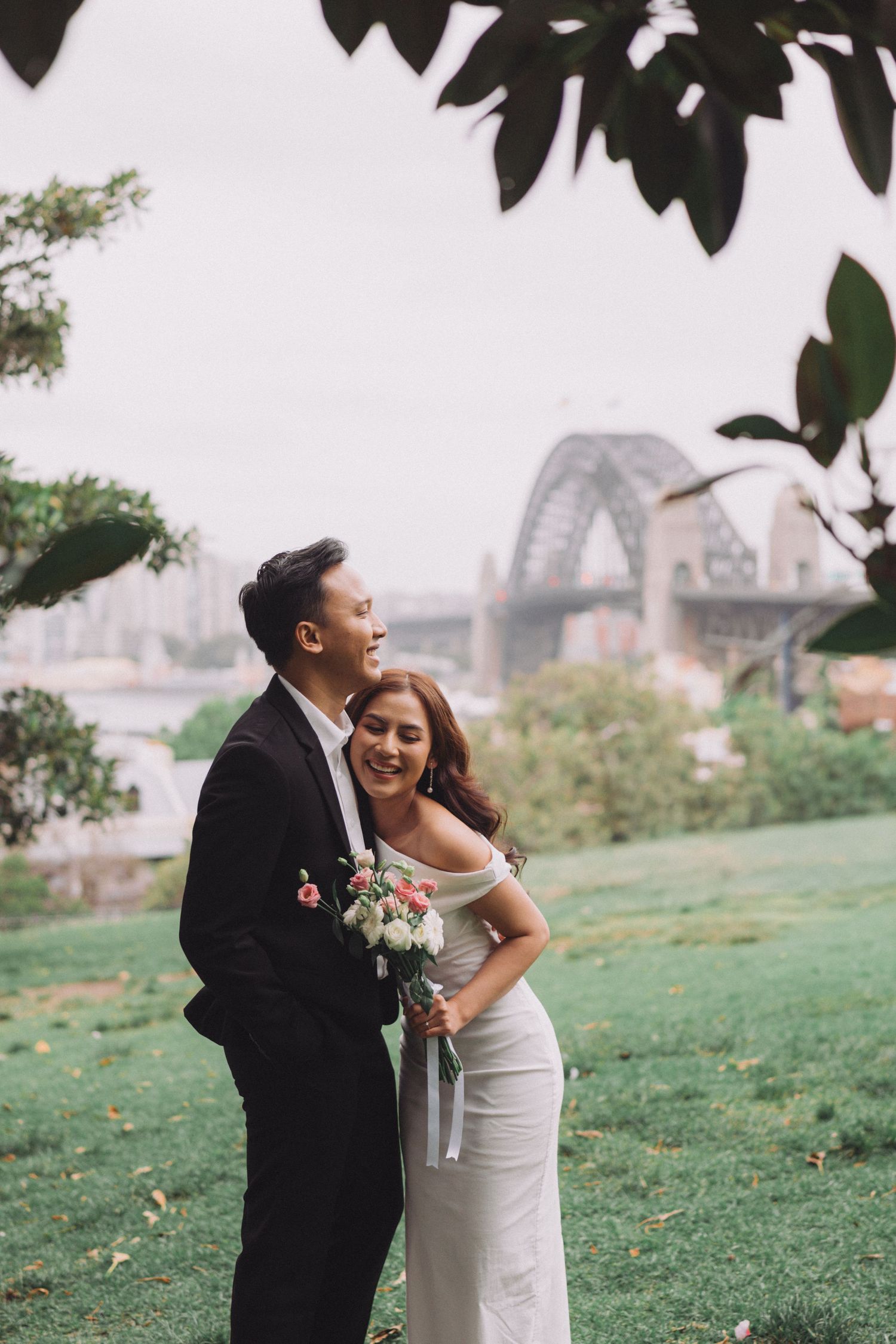 A happy couple shares a joyful moment together on a grassy hillside with a city skyline in the background.