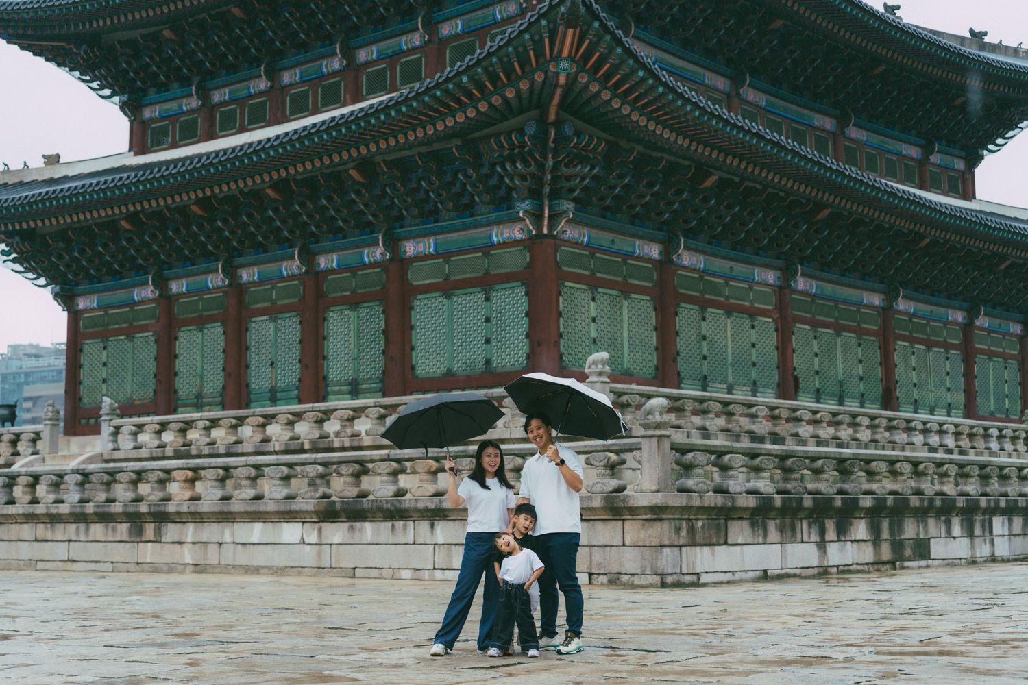 Traditional Korean palace buildings with ornate green roofs and decorative details stand against an overcast sky.