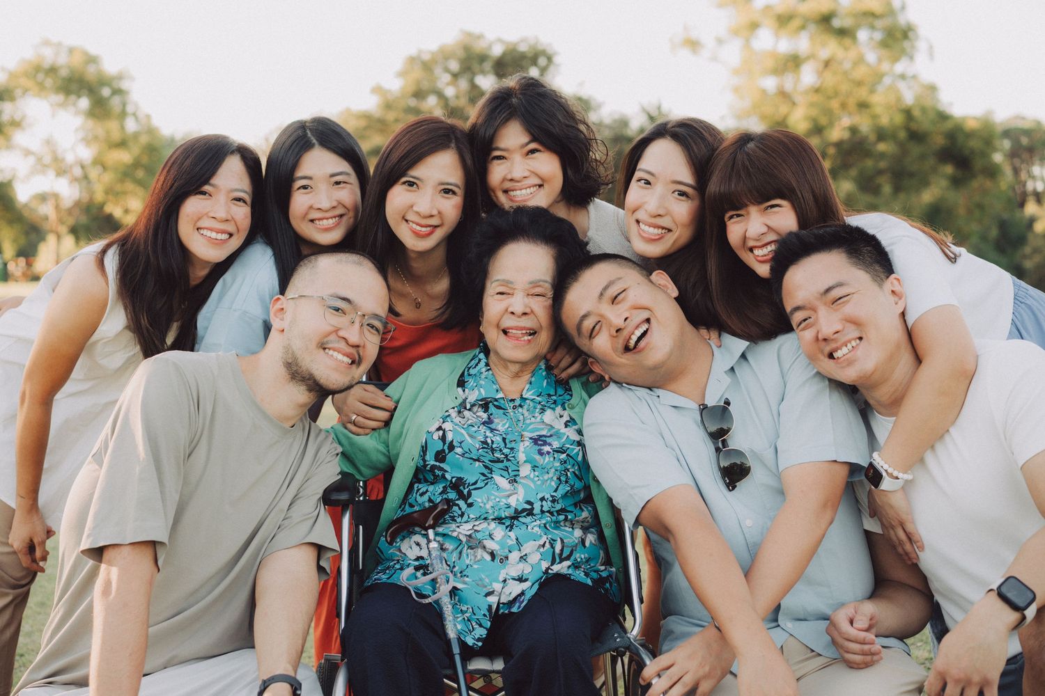 A joyful group poses together outdoors during a sunny day, creating a warm and candid moment.