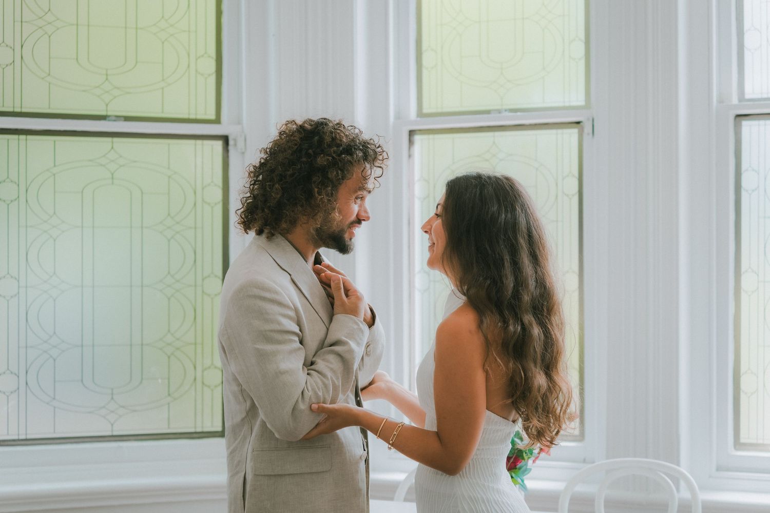 Romantic couple dancing together in a bright white room with large windows and soft natural lighting.