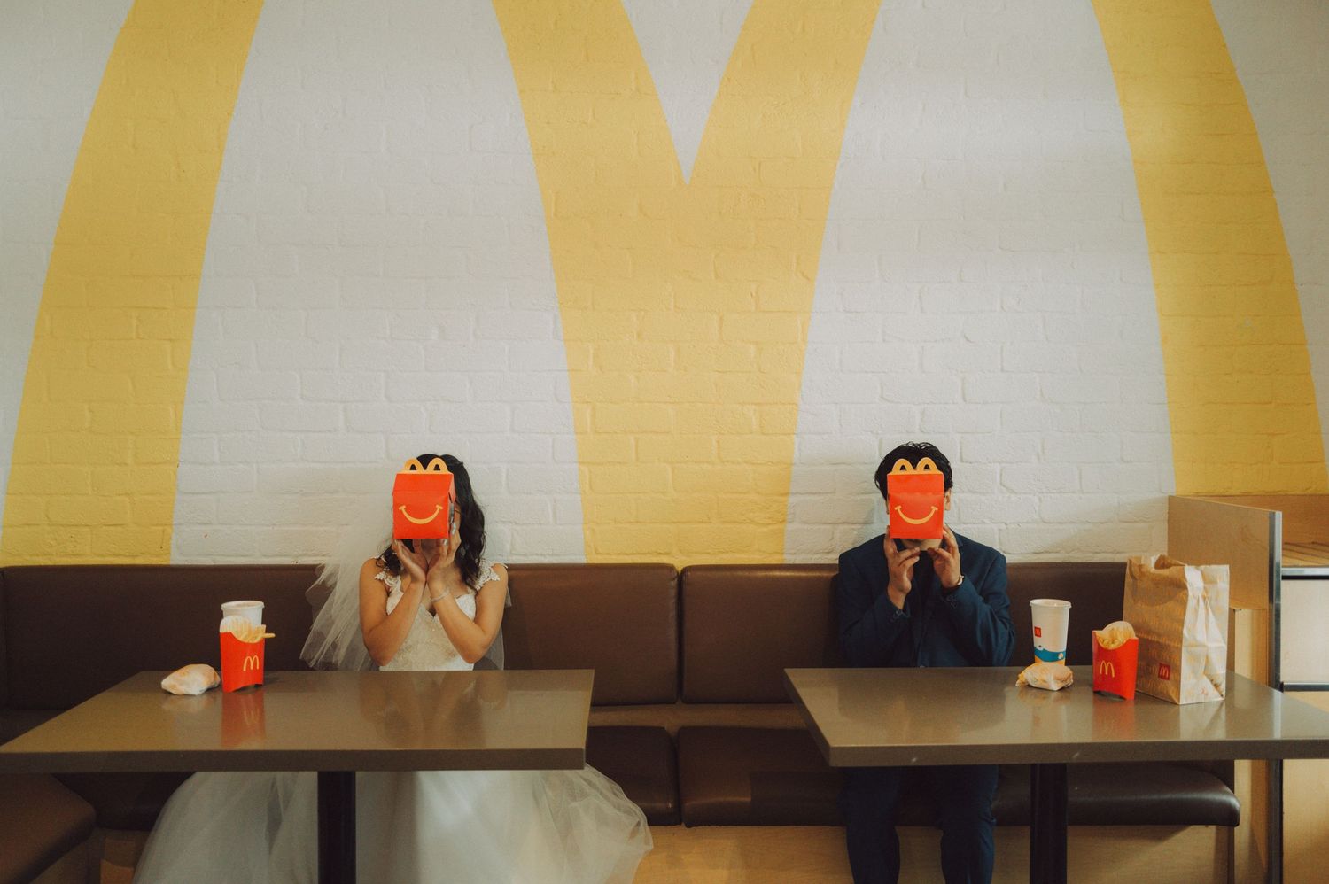 A person sits at a table with a bright orange drink in front of a yellow striped wall.