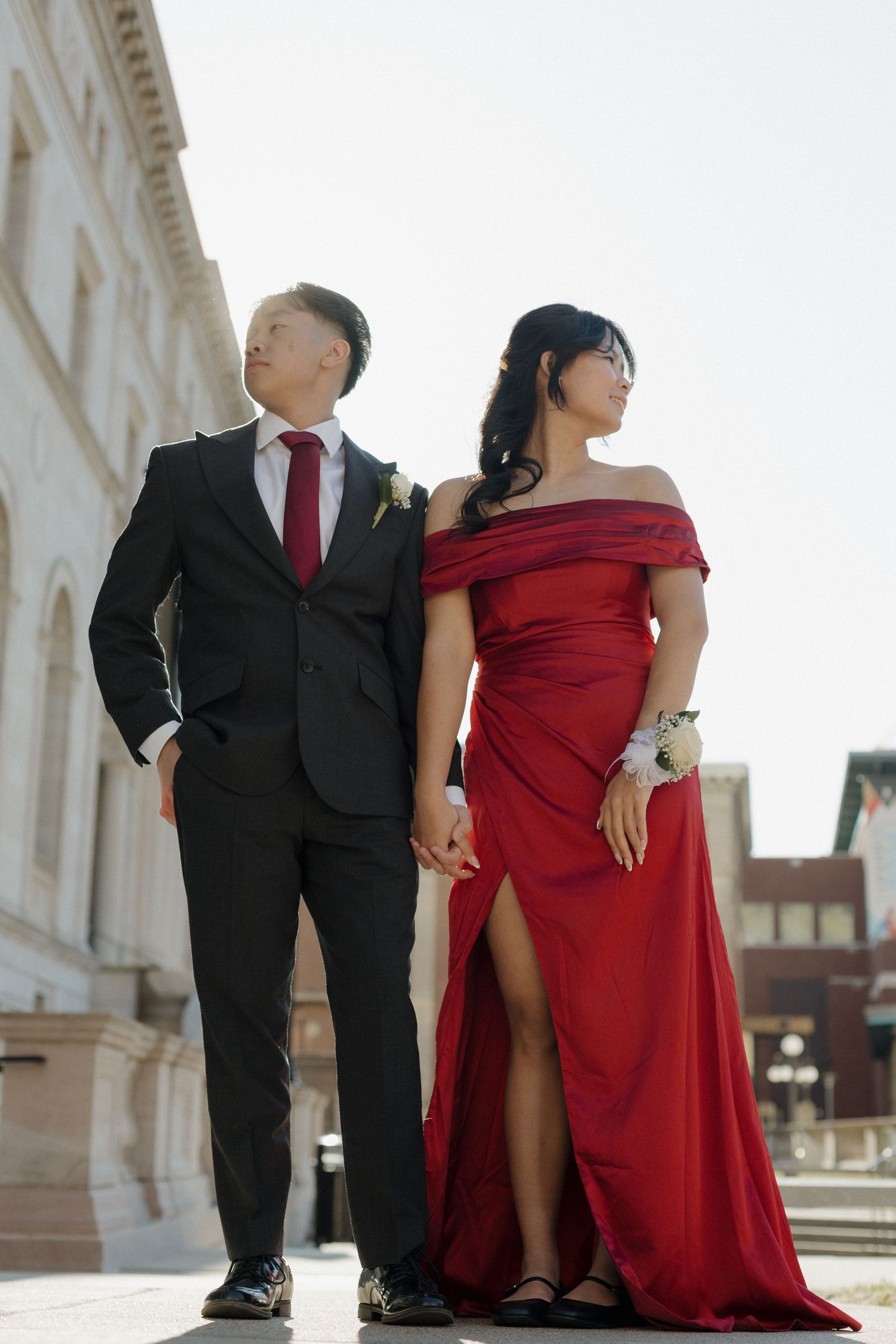 A couple in formal attire poses together, with the person wearing a red dress and another in a black suit.