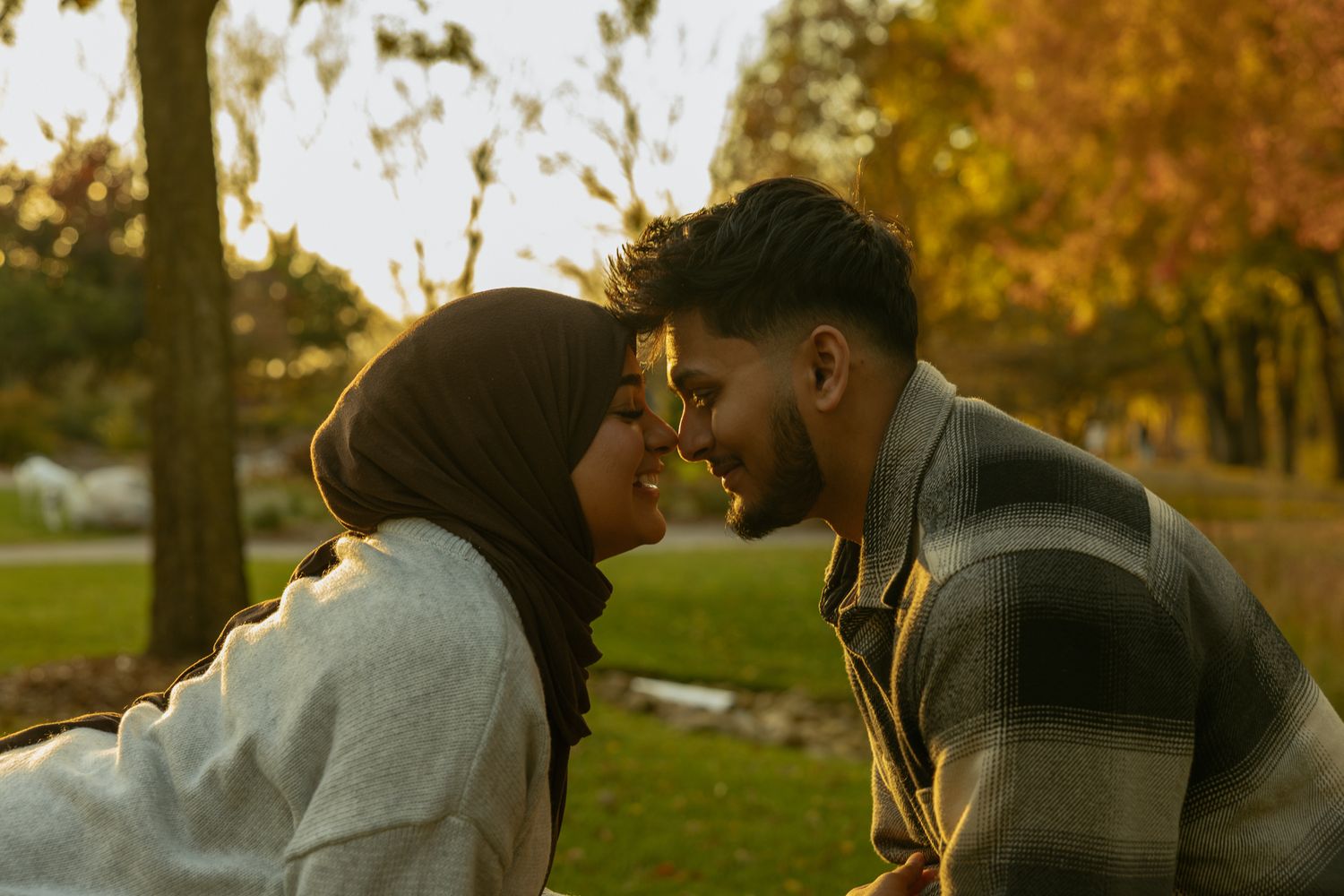 A romantic couple embraces and kisses in a park during golden autumn sunset lighting.