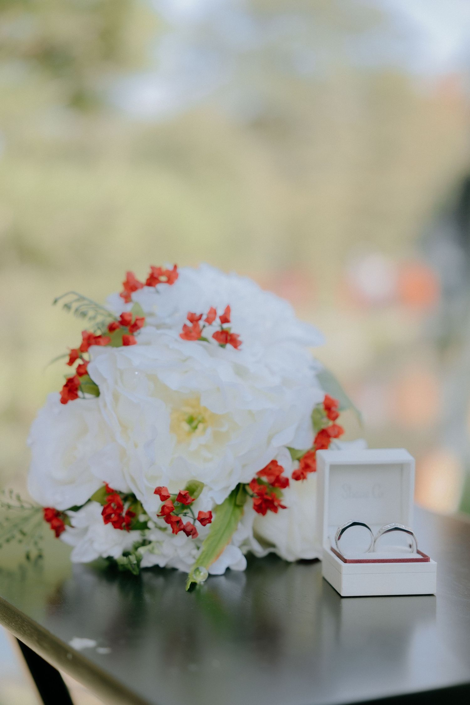 White carnations and red flowers arranged in a decorative display on a windowsill with soft natural lighting.