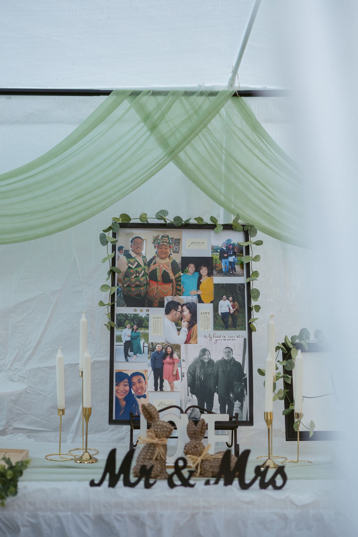 Wedding reception decor features a photo display with 'Mr & Mrs' sign, white draping, and candlesticks on a table.