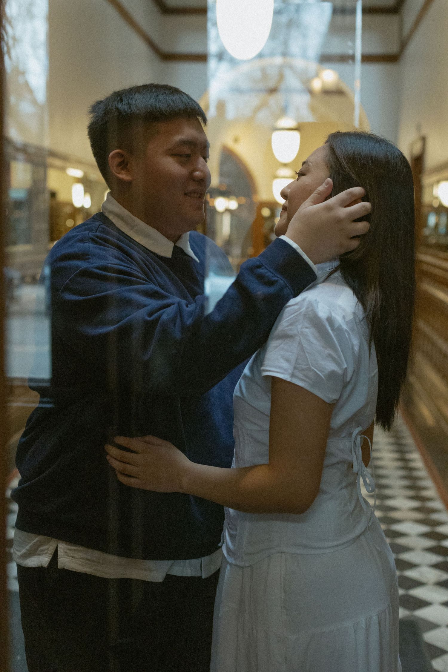 A tender romantic moment between a couple in a hallway with checkered floors and vintage lighting.
