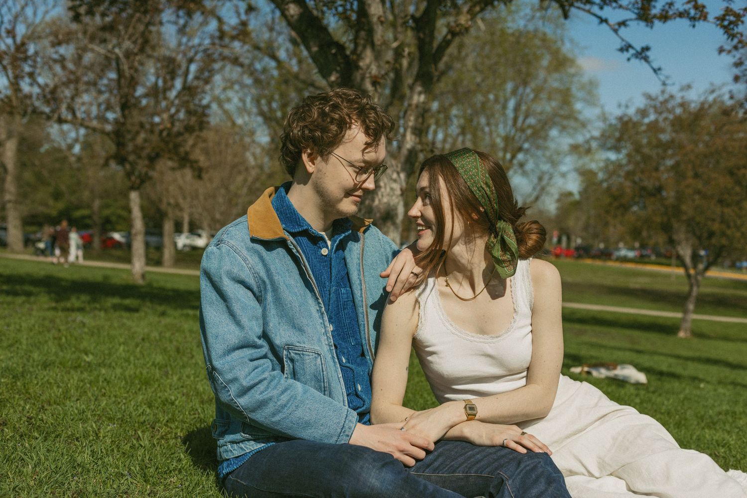 A couple shares a joyful moment together while sitting on a blanket in a sunny park setting.