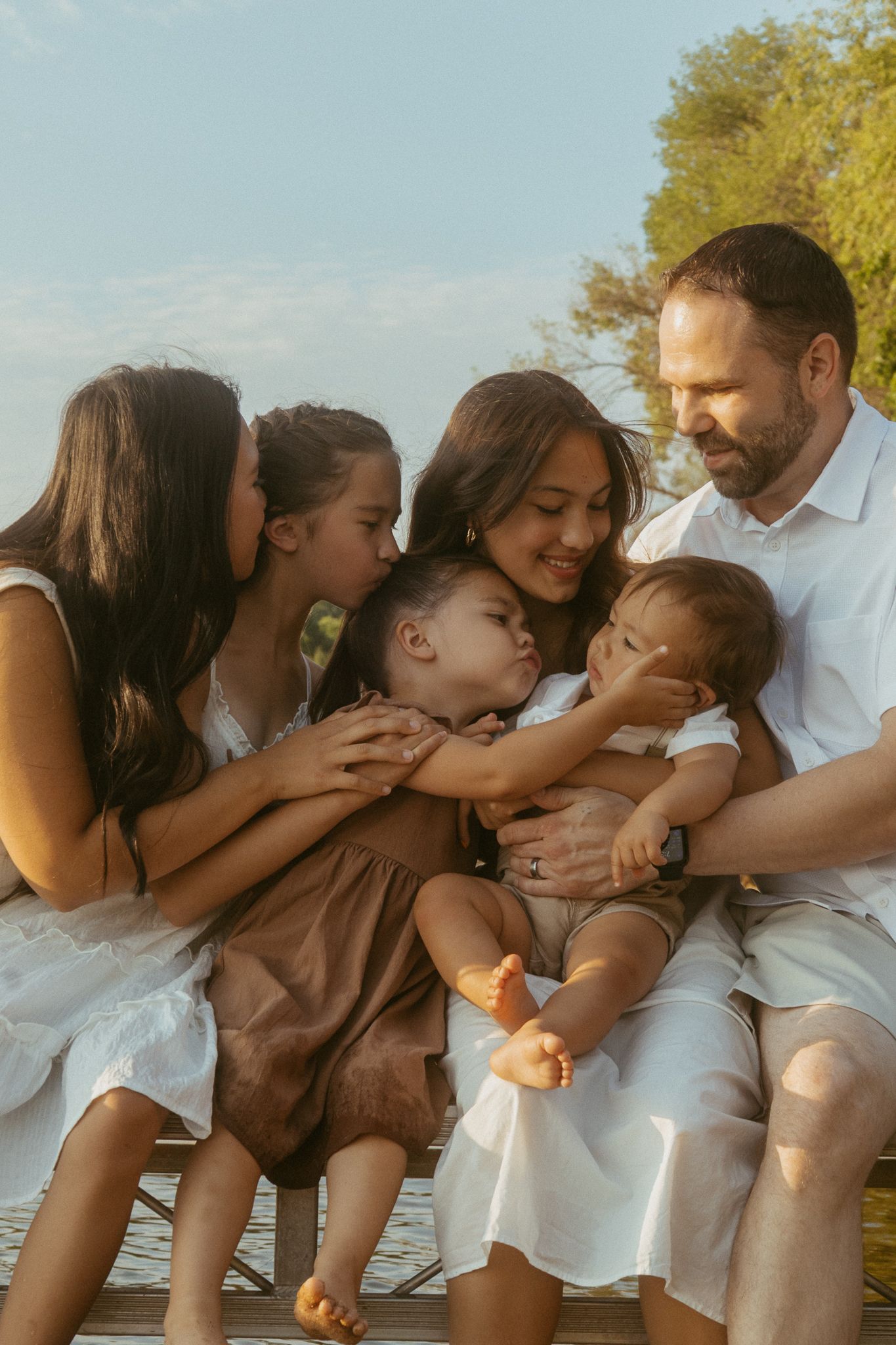 A family shares tender moments together on a sunny day while wearing white and dark clothing.