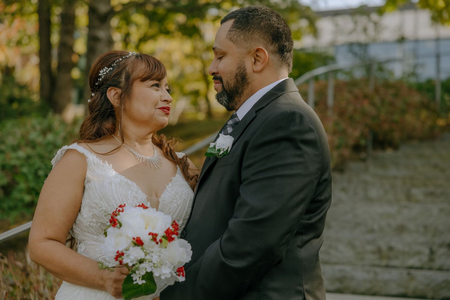 A romantic wedding couple shares an intimate moment in a garden setting while holding a floral bouquet.