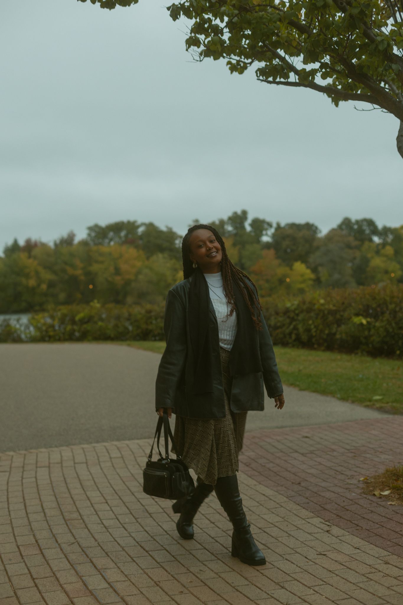 A person in dark clothing dances expressively on a brick pathway surrounded by autumn trees and foliage.