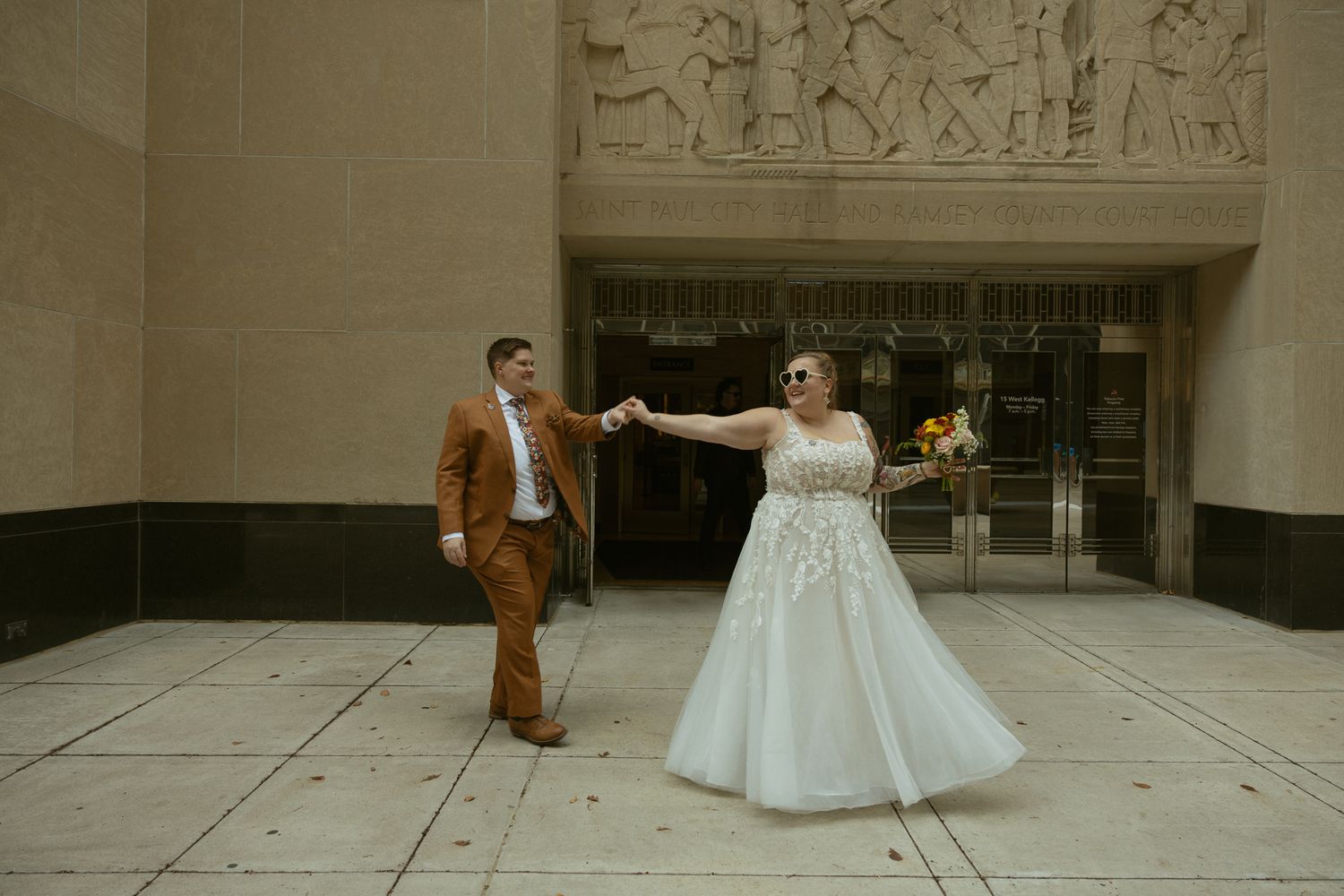 Wedding couple dancing and twirling in front of a stone building with classical architecture.