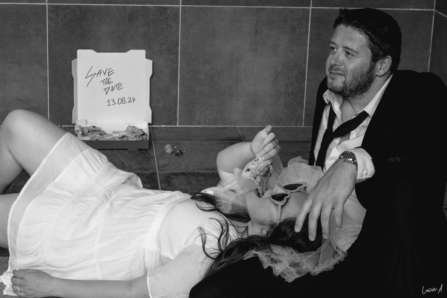 Photo en noir et blanc d'un couple avec une pancarte « Réservez la date » indiquant le 23.08.20, la femme allongée sur les genoux de l'homme