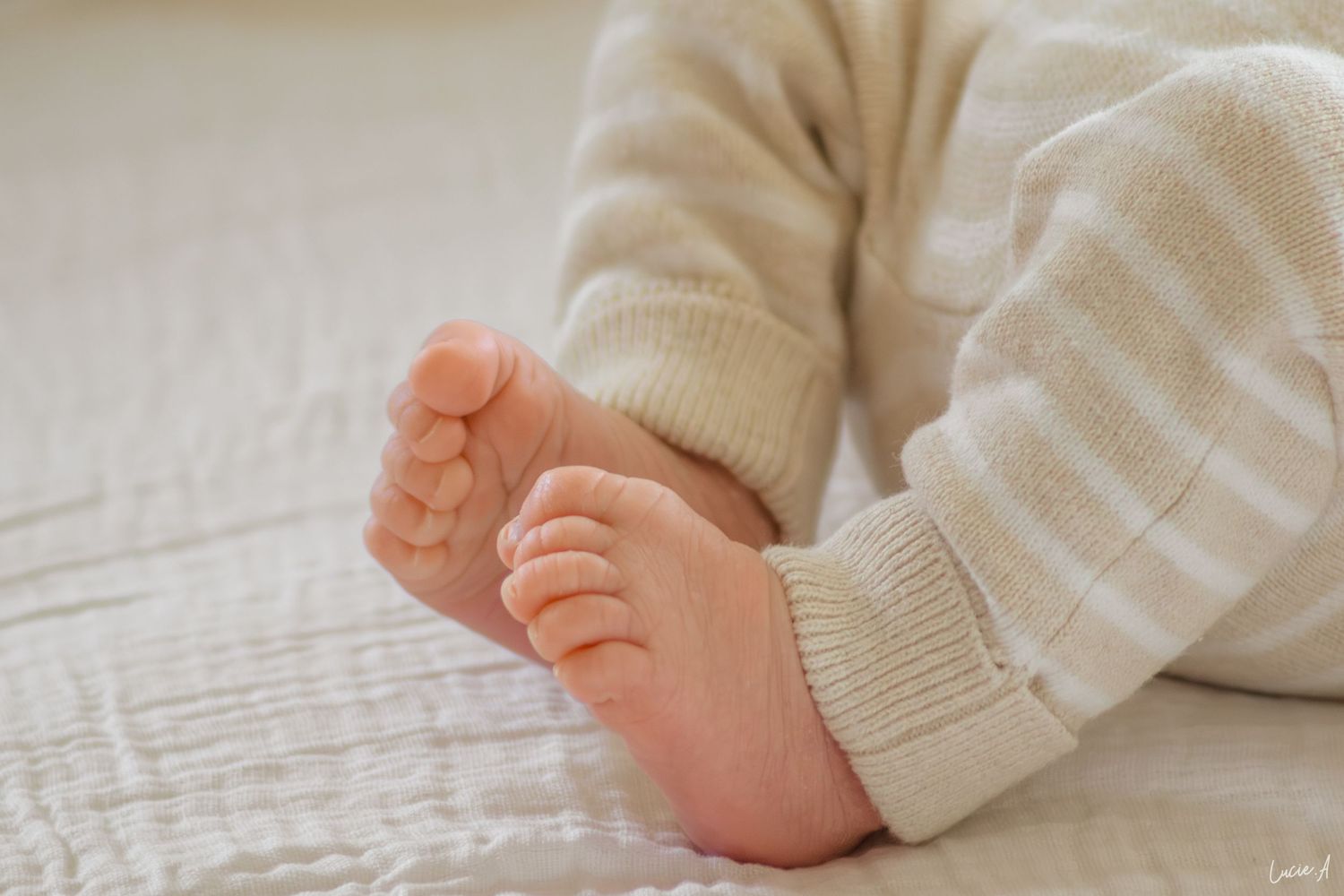 Gros plan sur de jolis pieds de bébé dans un body rayé reposant sur une couverture blanche texturée.