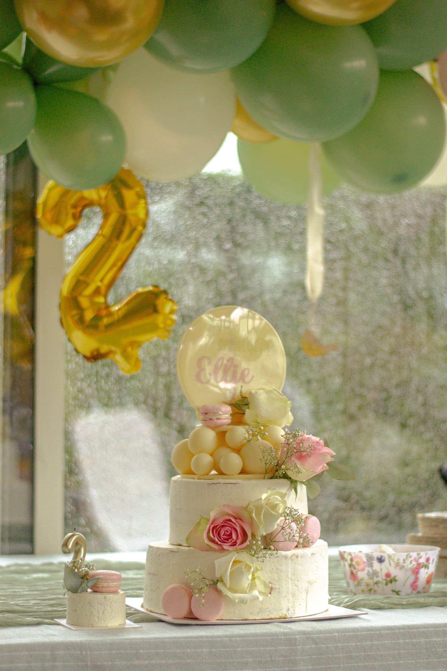 Un gâteau de mariage blanc orné de roses roses et de touches dorées est présenté sous des ballons, séance baptême à Ronchin