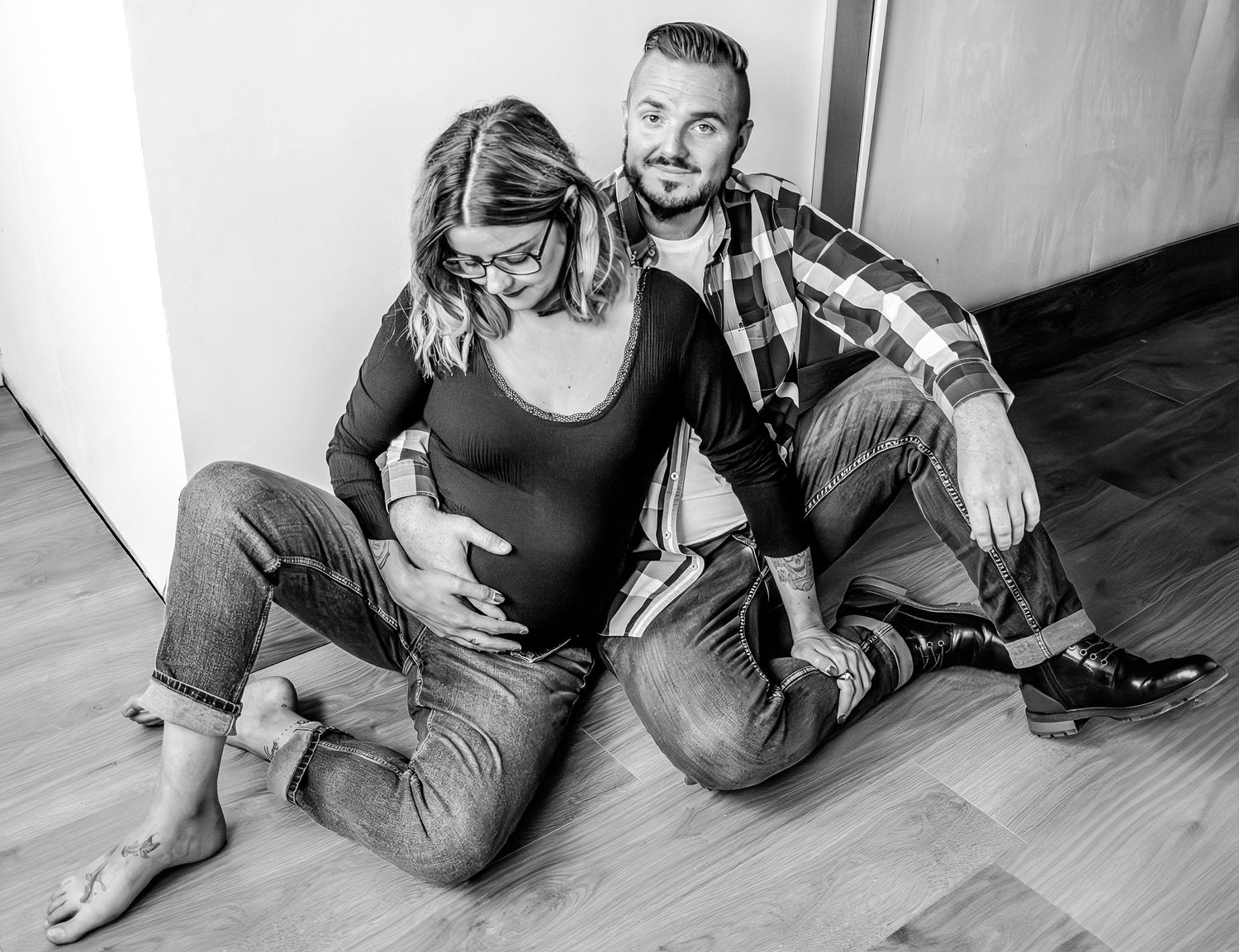 Portrait noir et blanc séance grossesse, couple assis, le futur père posant la main sur le ventre de la future mère, près de Lille