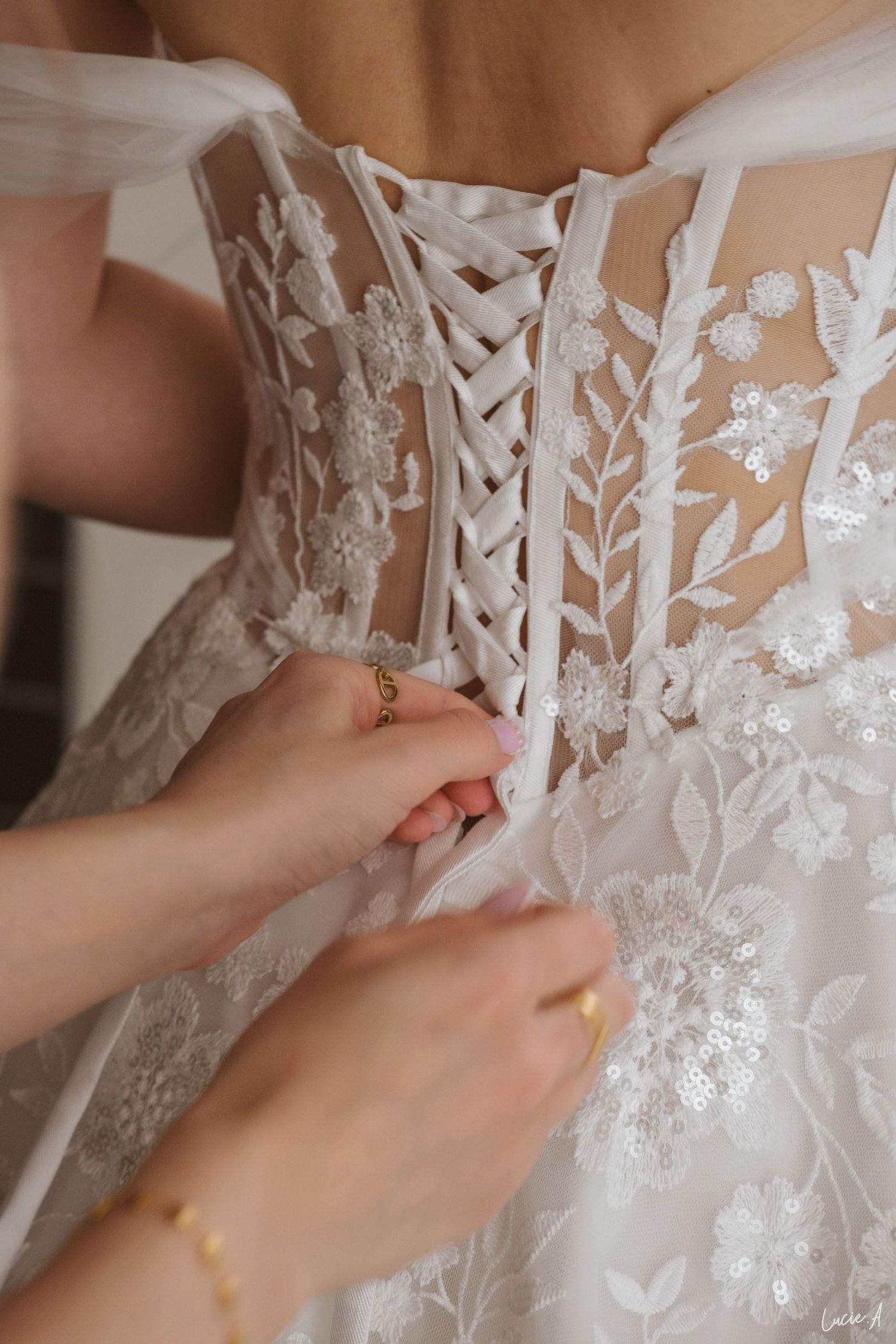 Le dos de la robe de mariée en dentelle, avec le laçage du corset, est noué par les mains des demoiselles d'honneur.