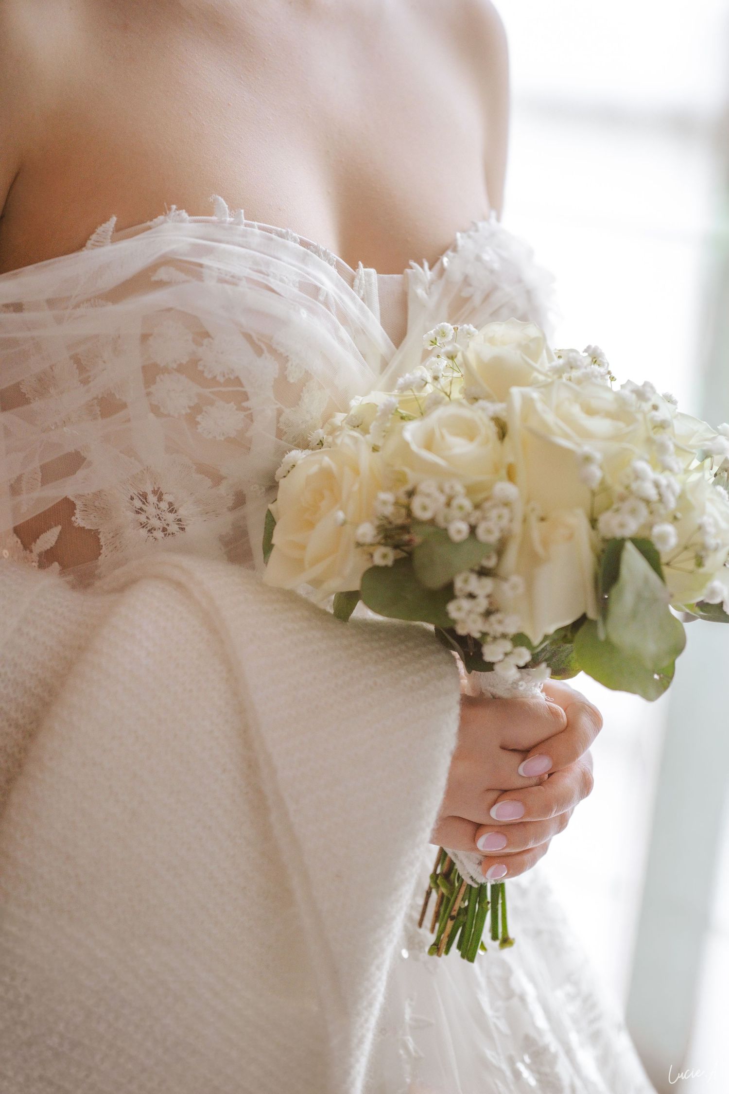 La mariée, vêtue d'une robe bustier en dentelle blanche, tient un élégant bouquet de roses crème et de gypsophile lors de son mariage.