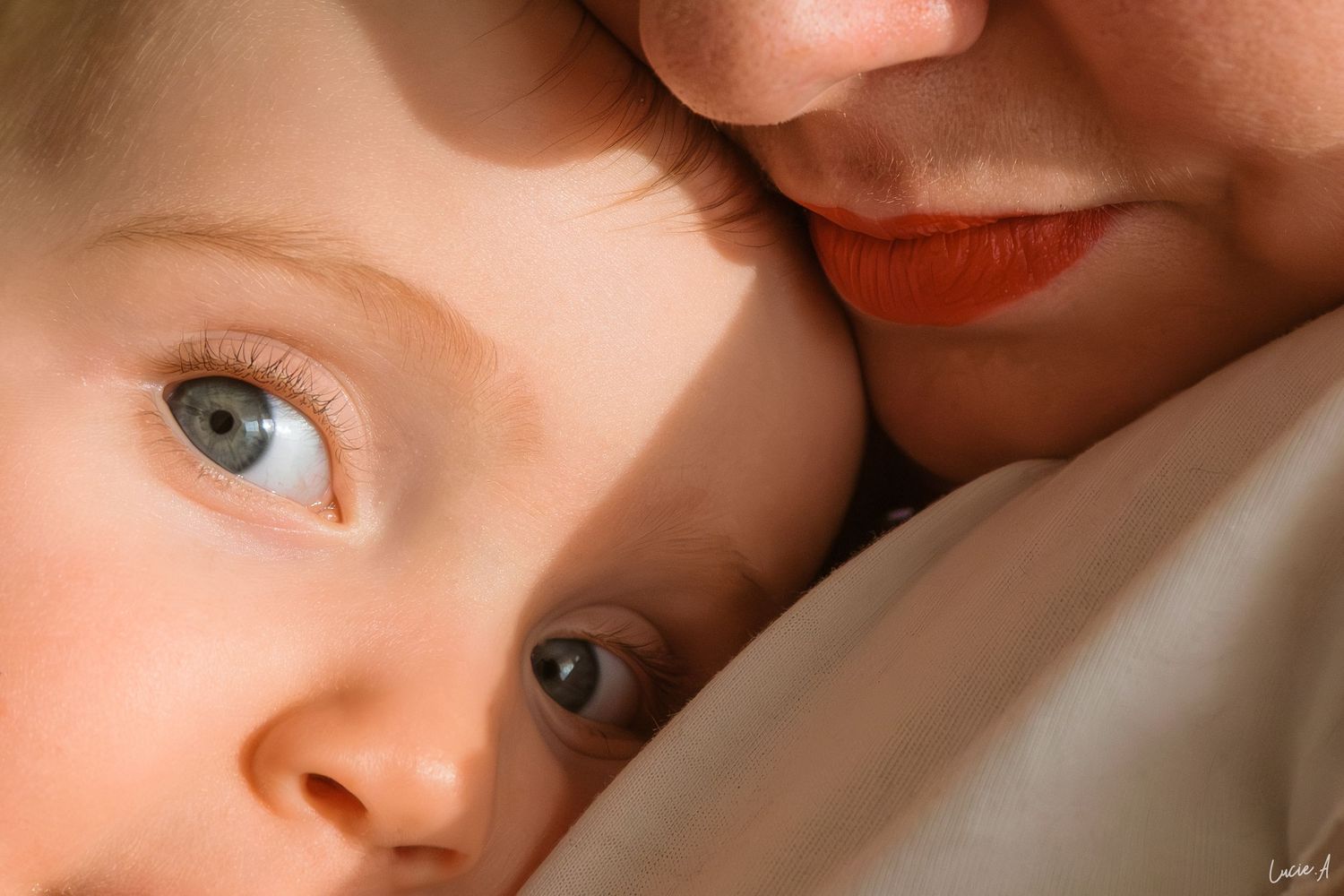 Gros plan sur un bébé aux yeux bleus blotti contre la joue de sa mère, partageant un tendre moment.