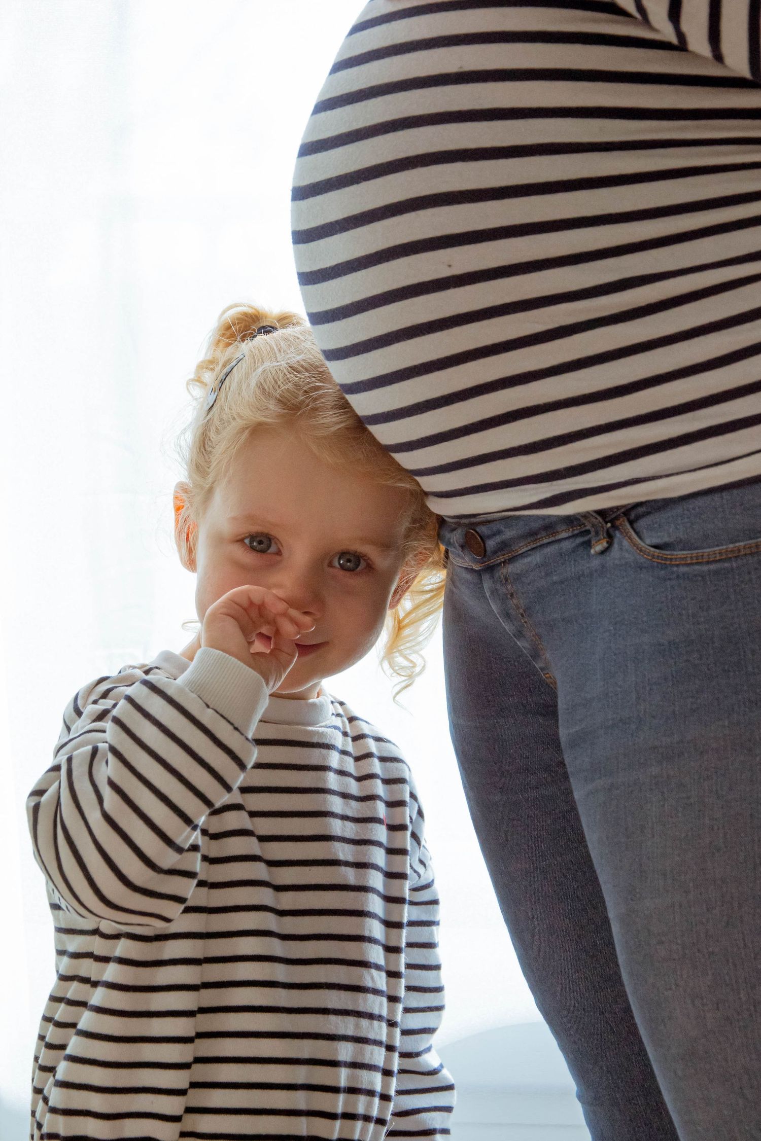 Portrait couleur famille et grossesse, la petite fille se tient sous le ventre de sa mère en posant sa tête dessus, prise à Ronchin