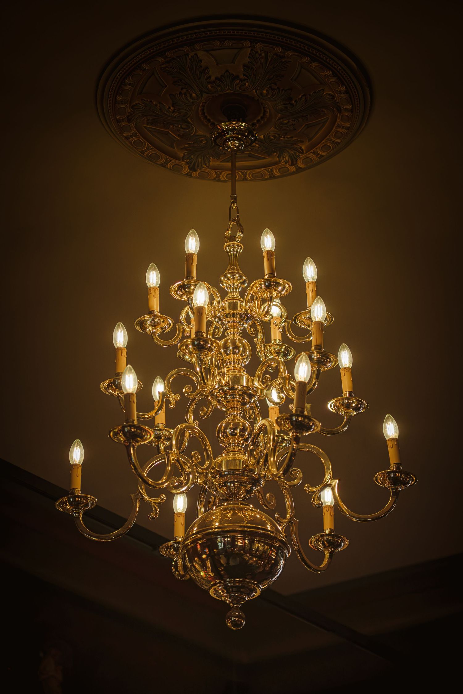 Lustre doré orné, avec des ampoules de style bougie suspendues à un médaillon décoratif au plafond, diffusant une douce lumière ambrée.