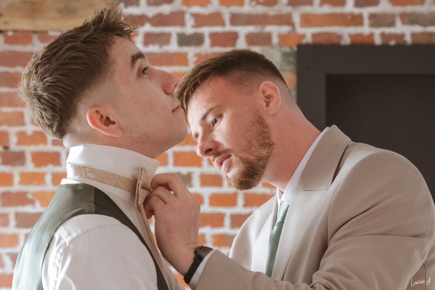 La futur marié et son témoins partagent un moment d'intimité, l'un ajustant la cravate de l'autre lors des préparatifs de mariage.