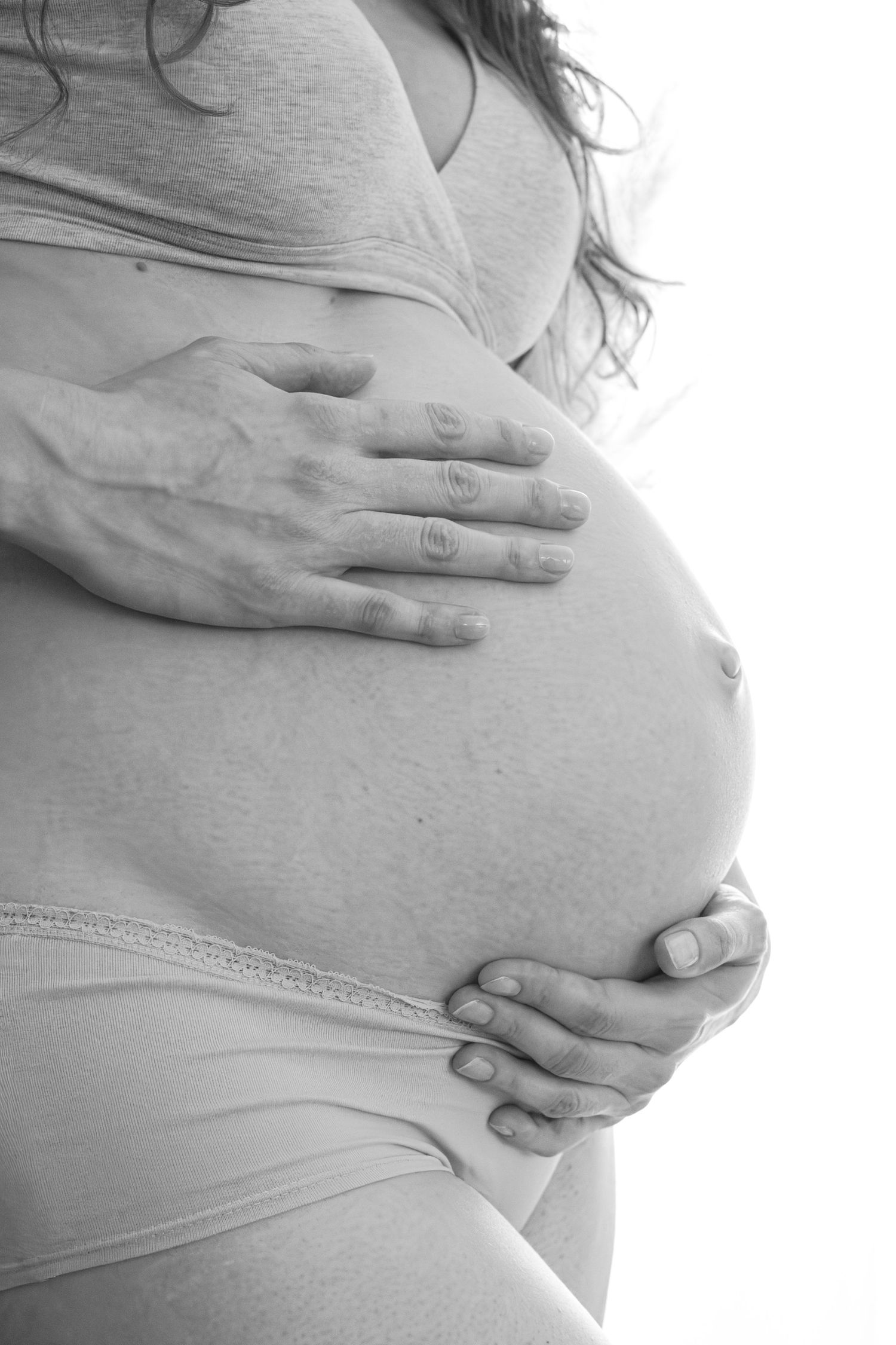 Black and white photo of a pregnant woman cradling her bare baby bump with both hands.