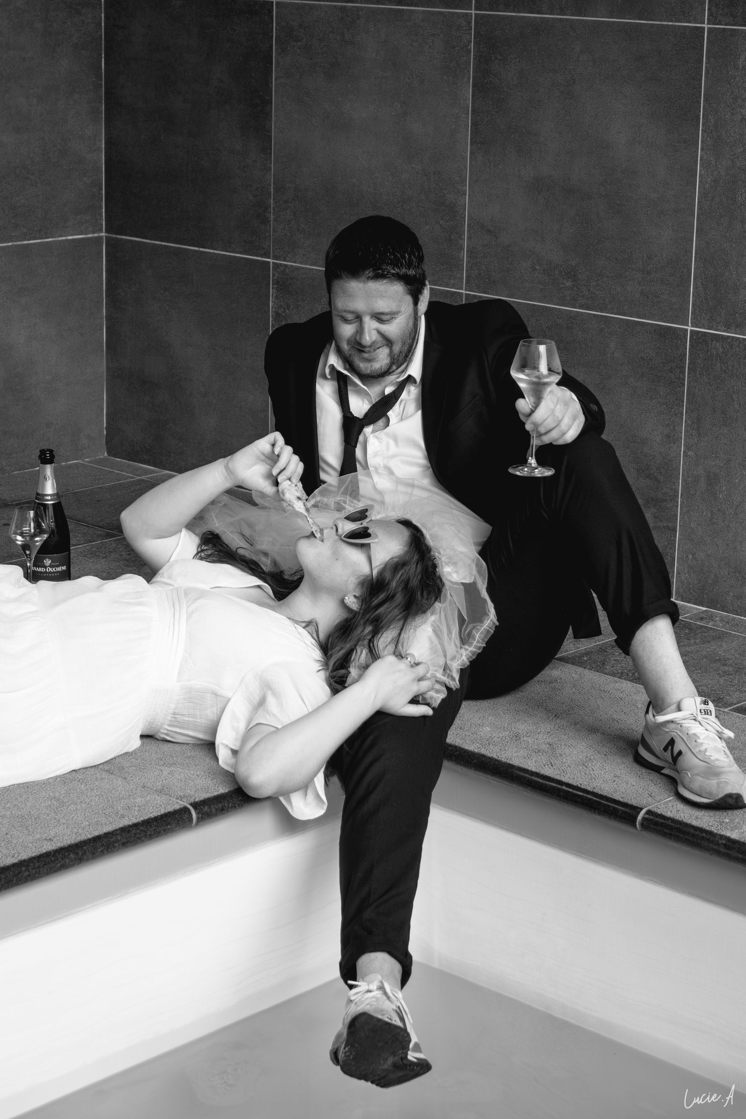 Photo en noir et blanc d'un couple en tenue de soirée se détendant au bord d'une piscine, partageant un verre de vin pour un save the date;